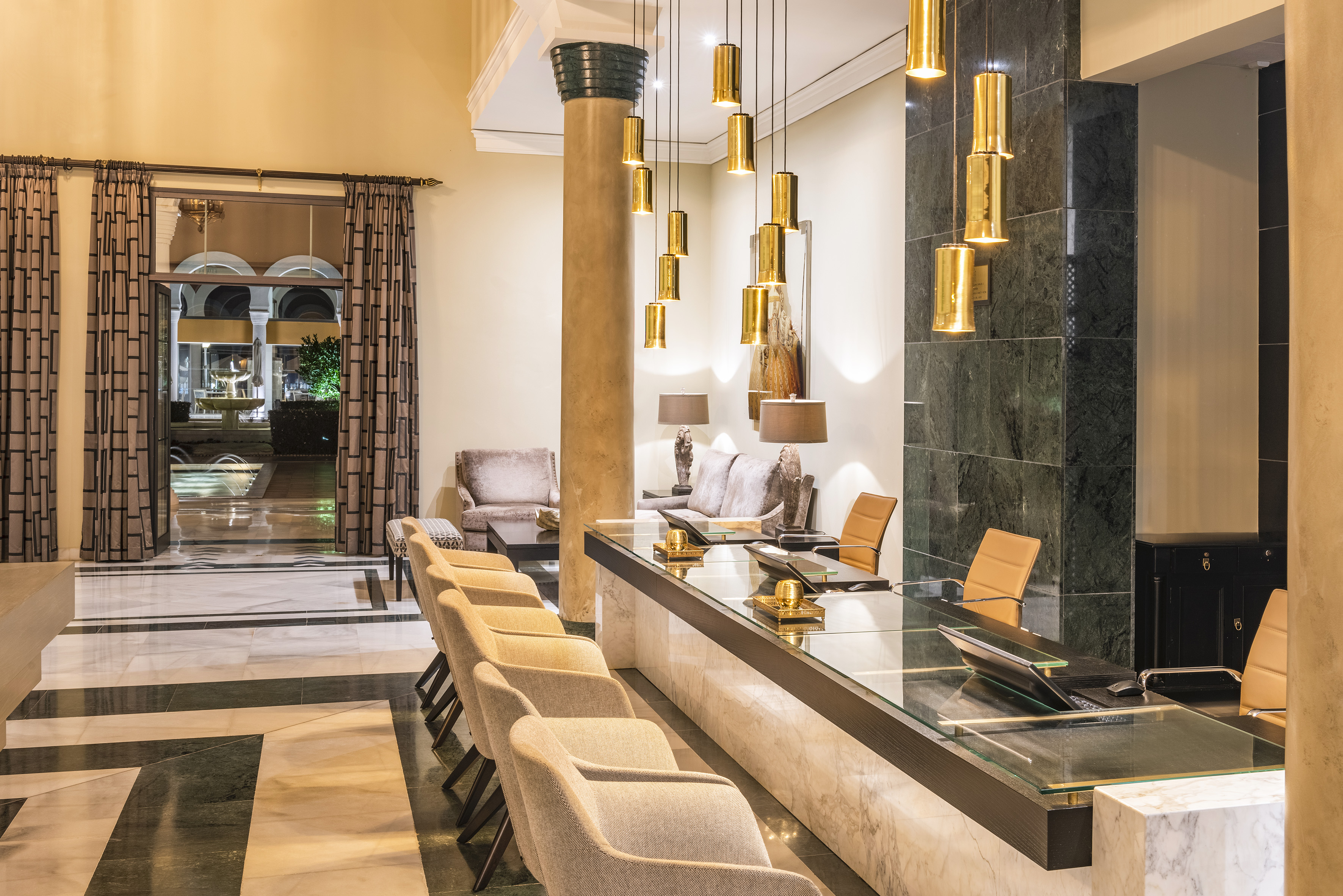 Luxury hotel lobby with marble reception desk, gold pendant lights, and patterned floor.