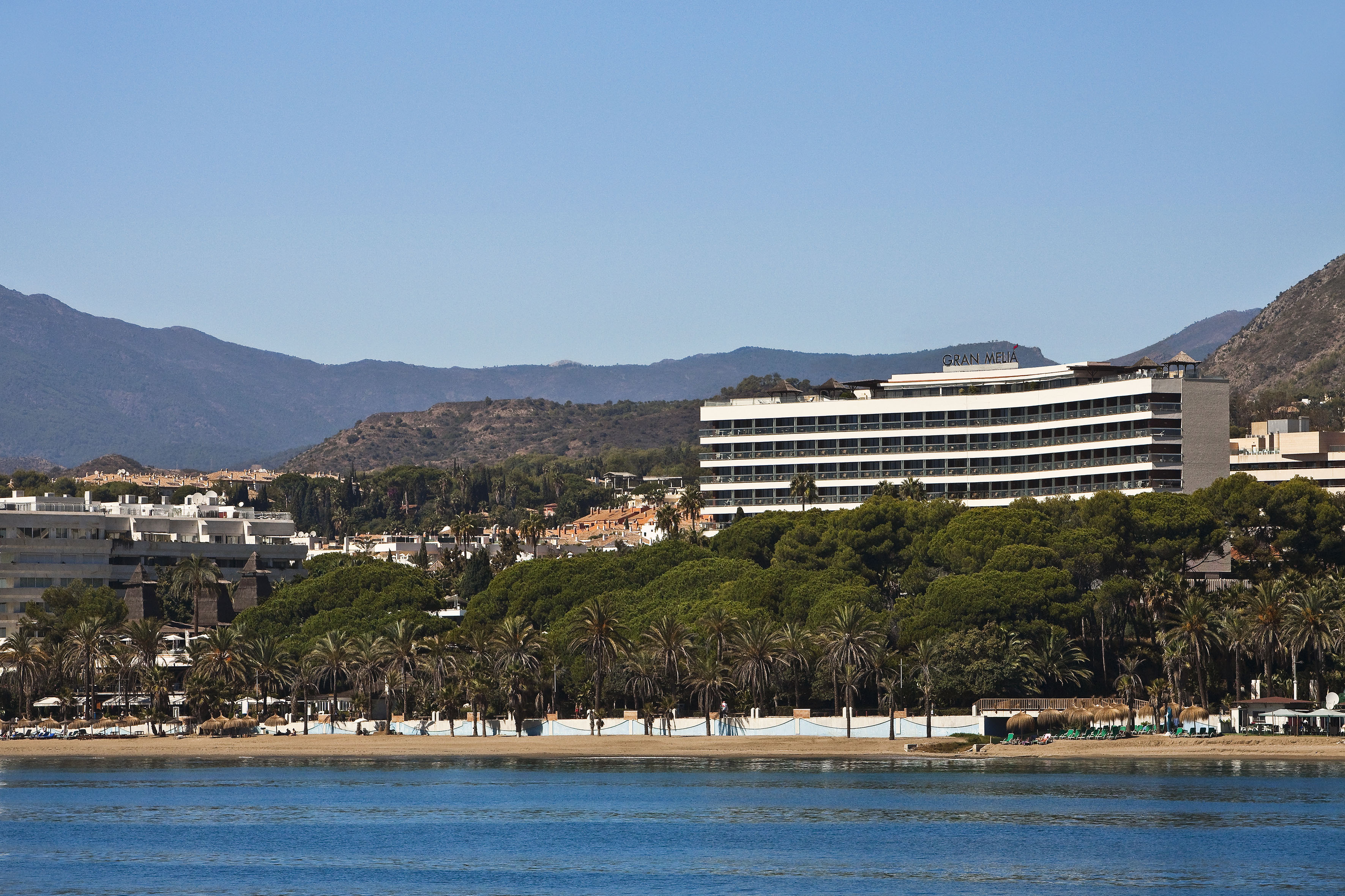 Gran Melia hotel by beach with palm trees, blue sea, and distant mountains.