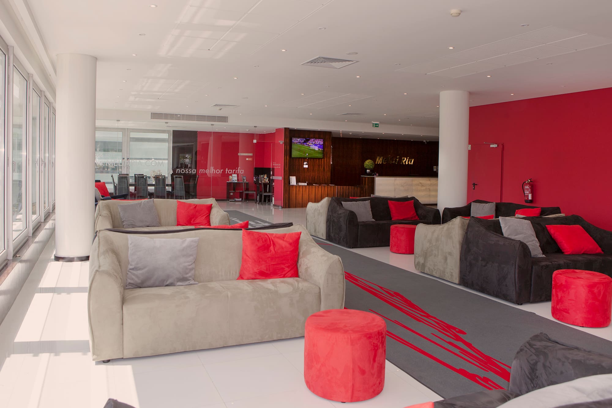Modern hotel lobby with grey sofas, red cushions, reception area, and large windows.
