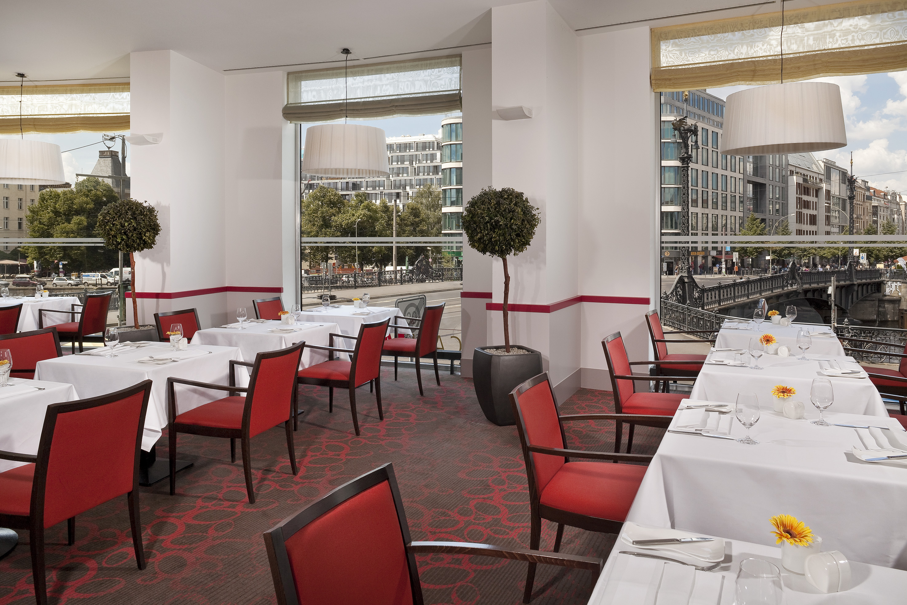 Restaurant interior, red chairs, white tables, city canal view windows. - Ontbijtbuffet, Show cooking - Meliá Berlin, Berlijn