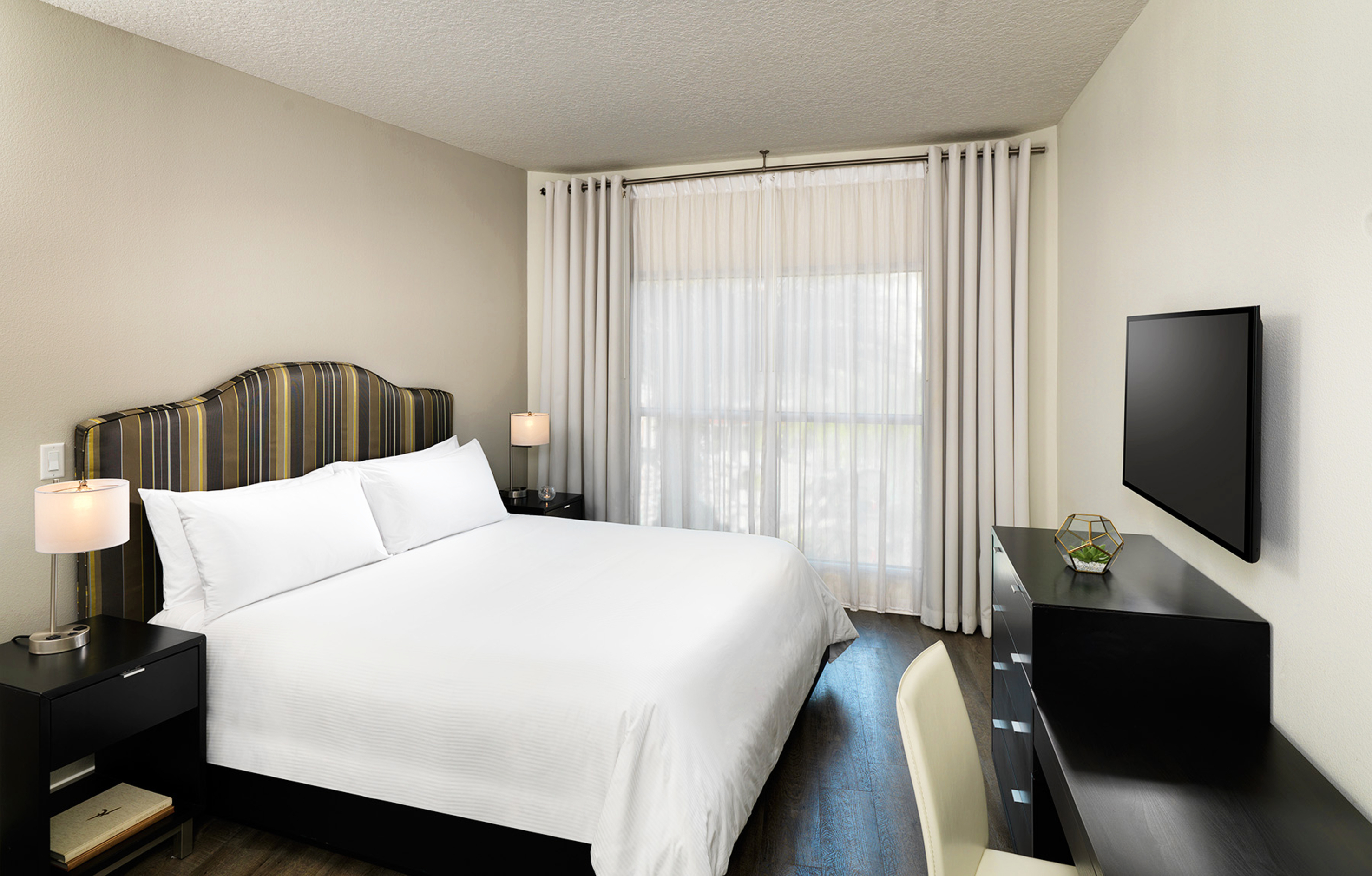 Modern hotel bedroom with white bed, striped headboard, nightstands, and wall-mounted TV. - Accessible Room - Meliá Orlando Celebration, Orlando