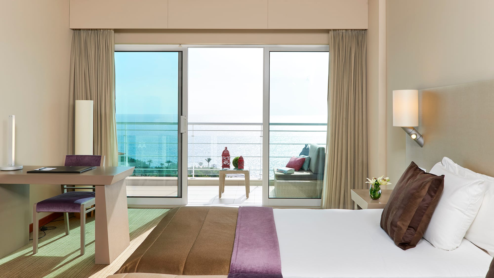 Hotel bedroom with sea view balcony, bed, and workspace.