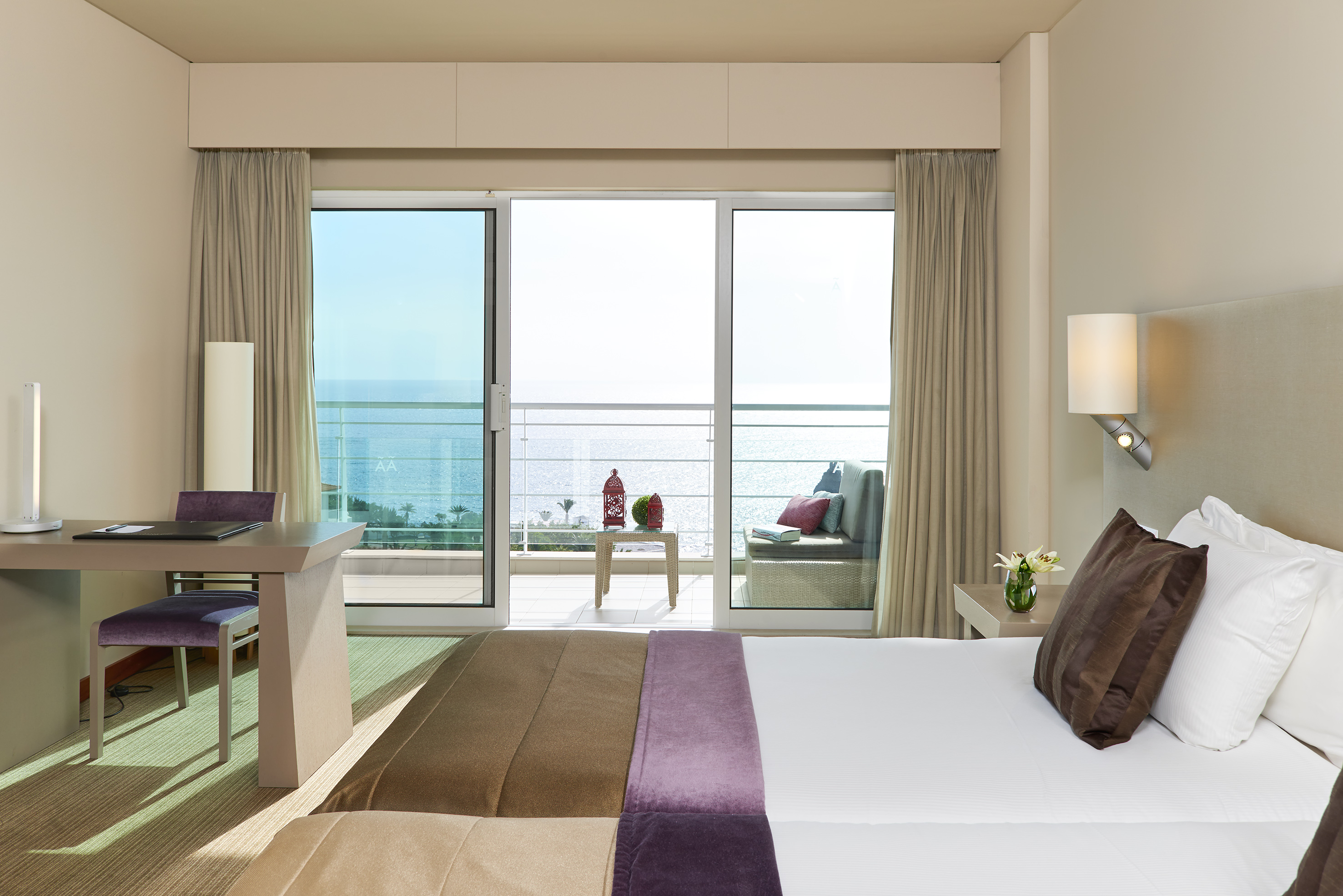 Hotel bedroom with sea view balcony, bed, and workspace.