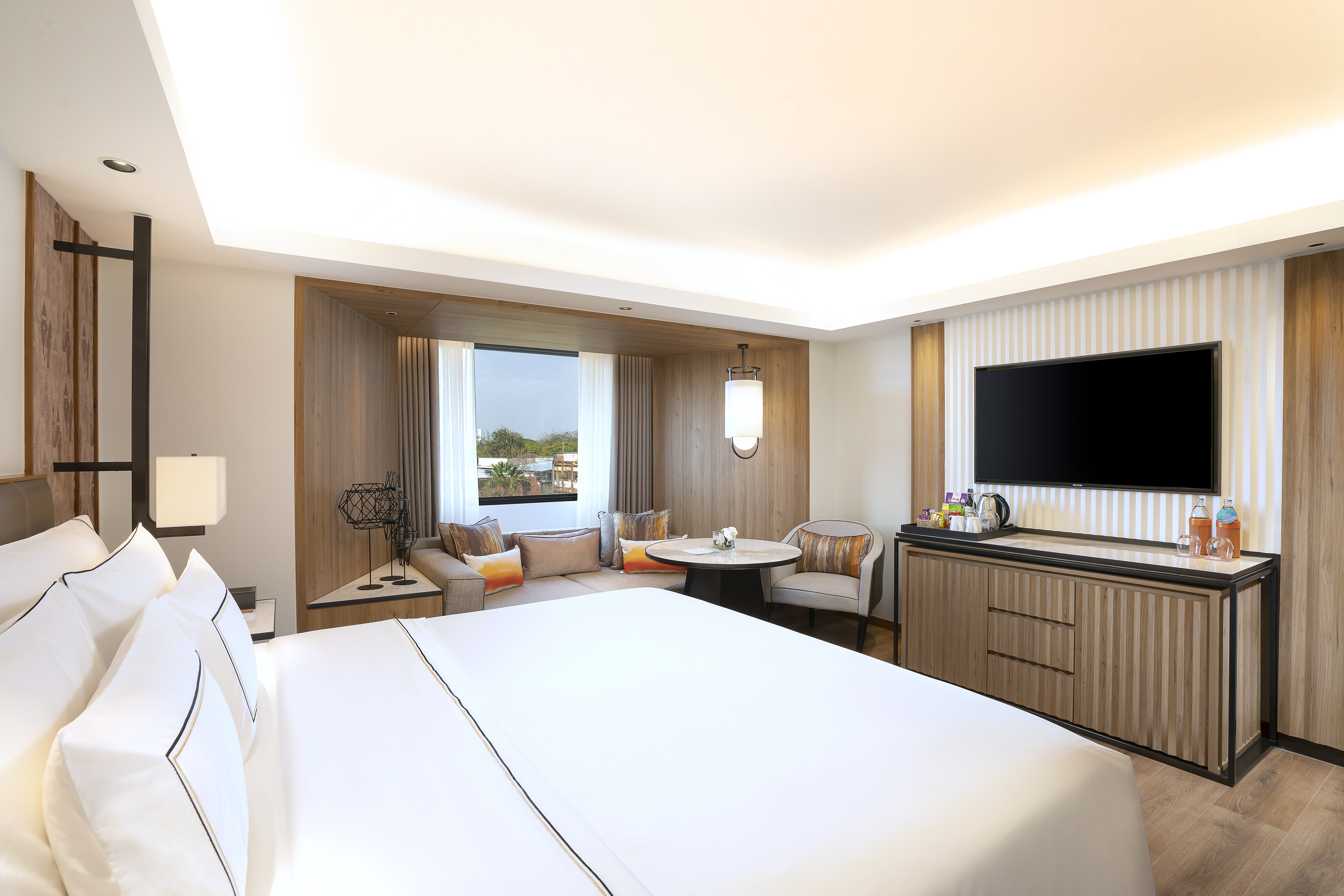 Spacious modern hotel room with a comfortable bed, window seating, and TV.