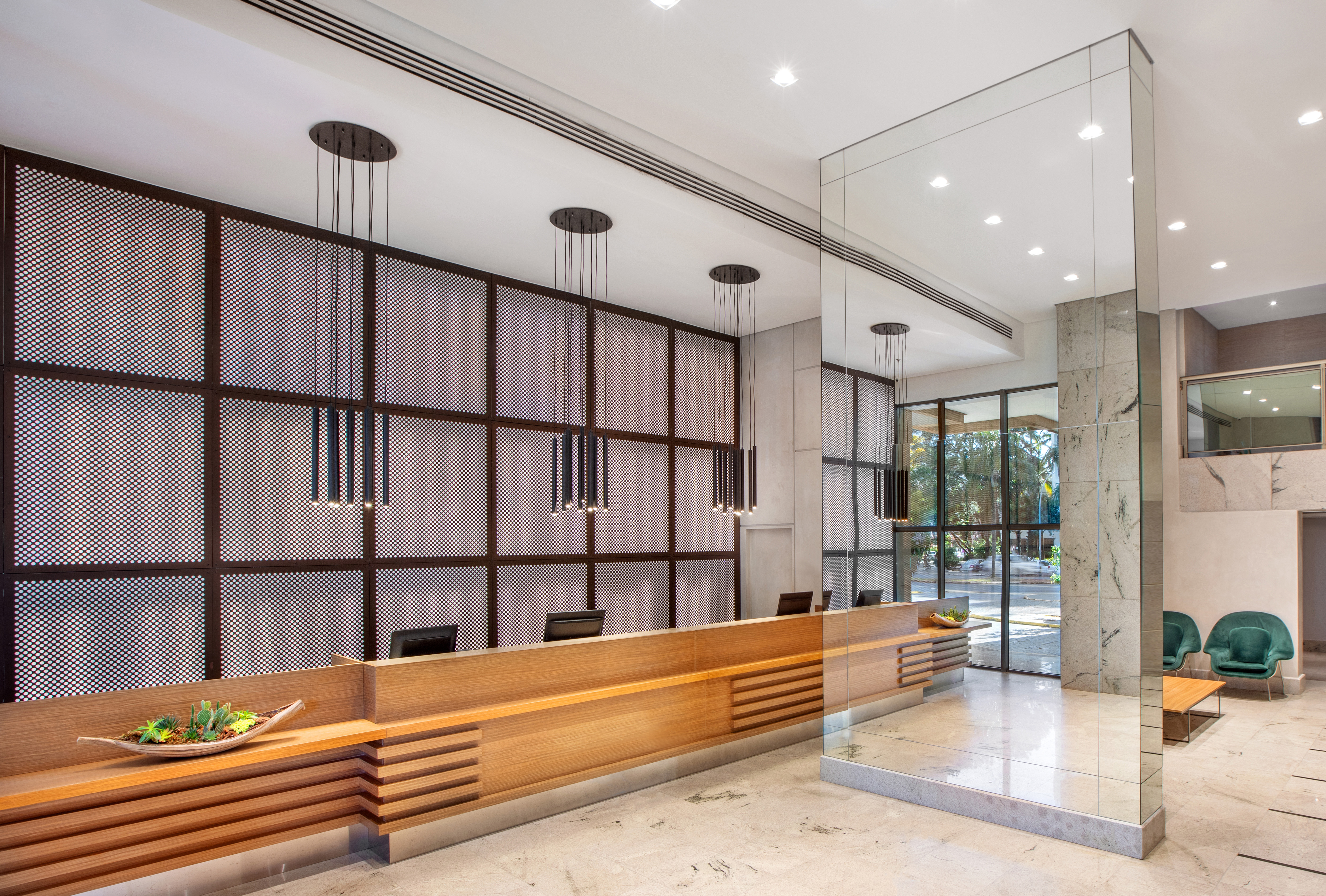Modern hotel reception with long wooden desk, perforated screen, and pendant lights.