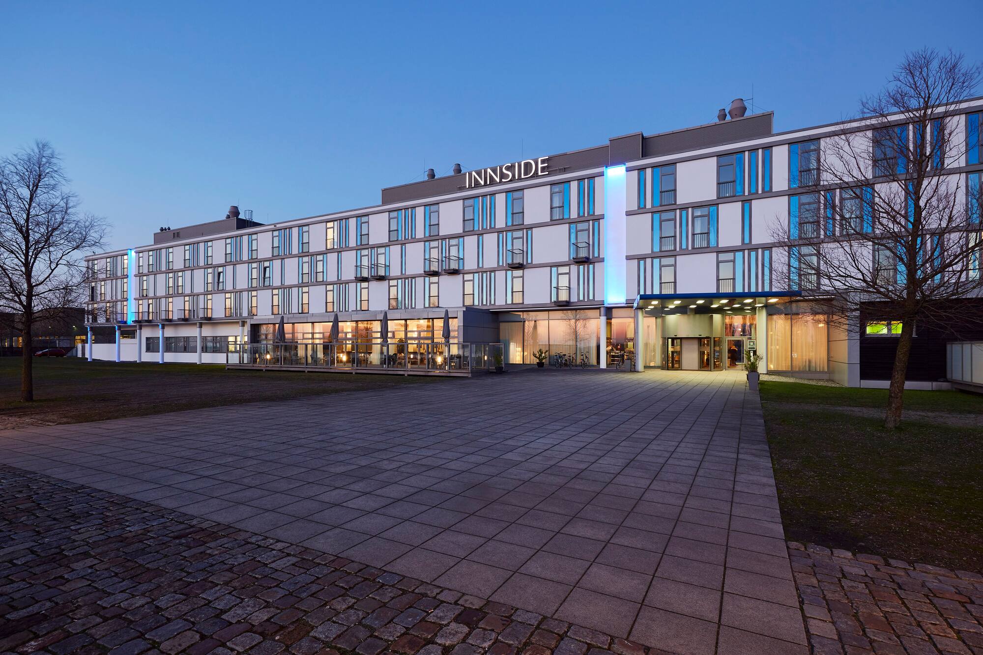 Modern INNSIDE hotel exterior at dusk, illuminated facade and entrance.