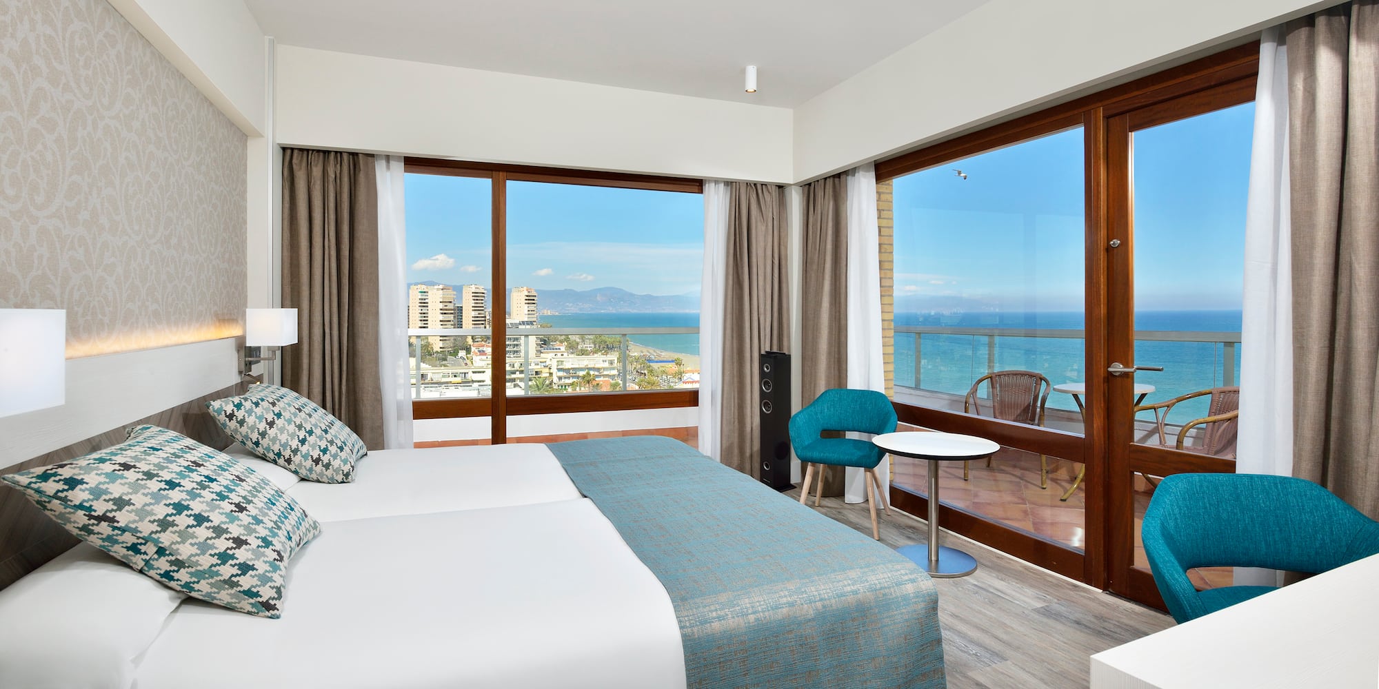 a room with a bed and a table and chairs and a balcony with a view of the ocean