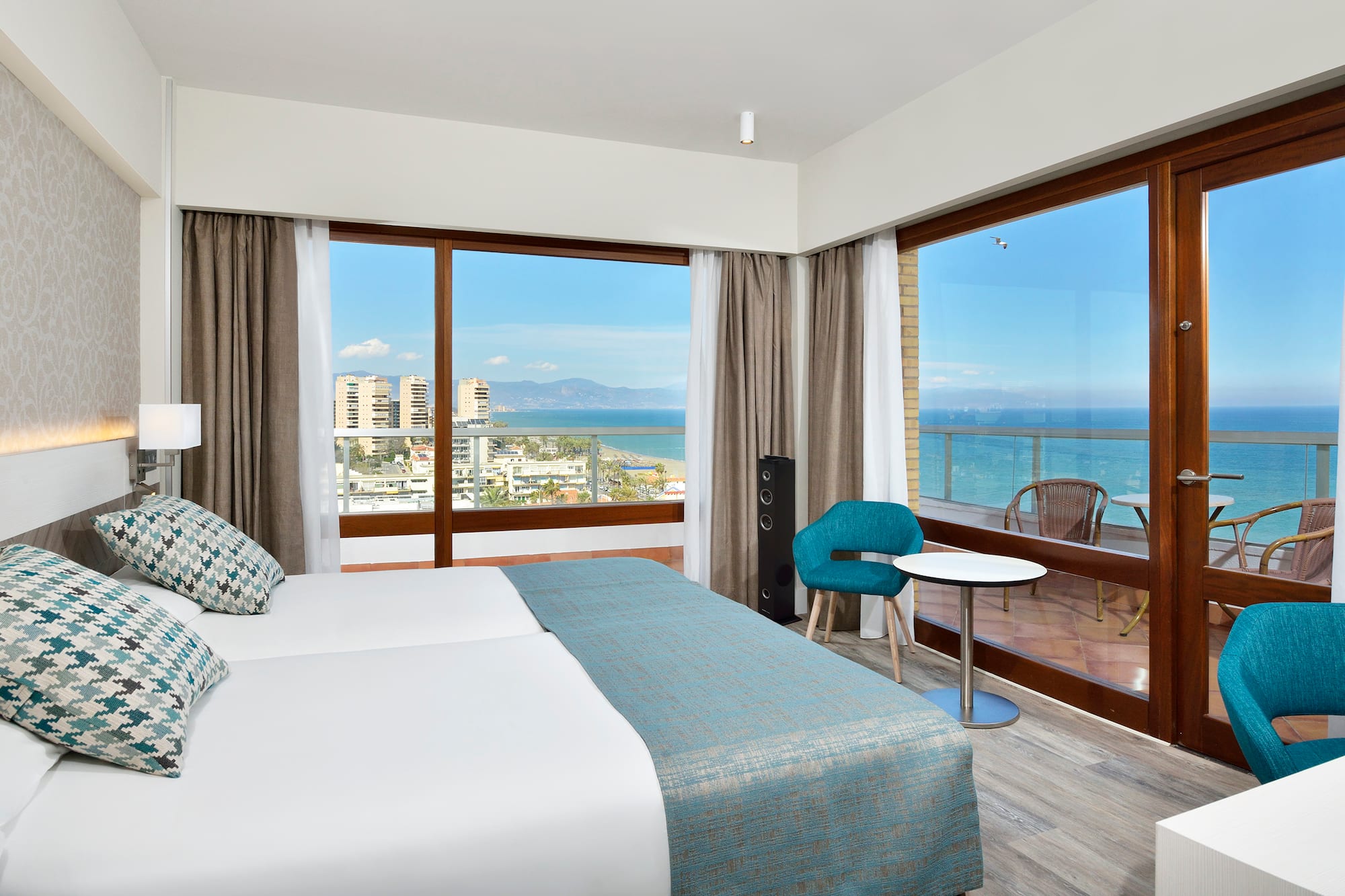 a room with a bed and a table and chairs and a balcony with a view of the ocean