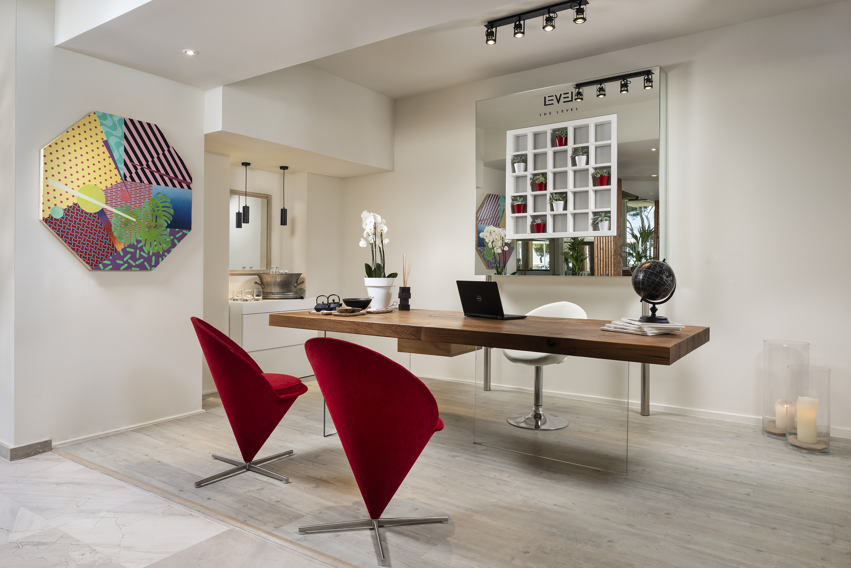 Modern office with wooden desk, red chairs, geometric art, and The Level mirror.