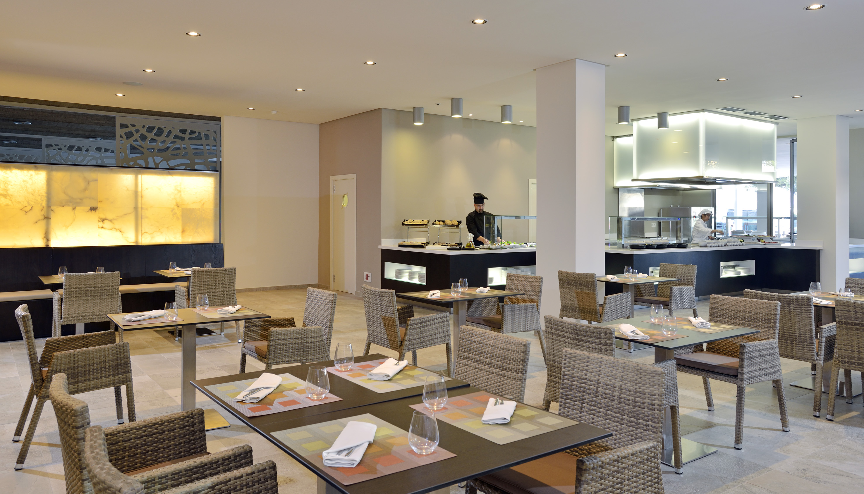 Modern restaurant with buffet, chefs, and set wicker dining tables.