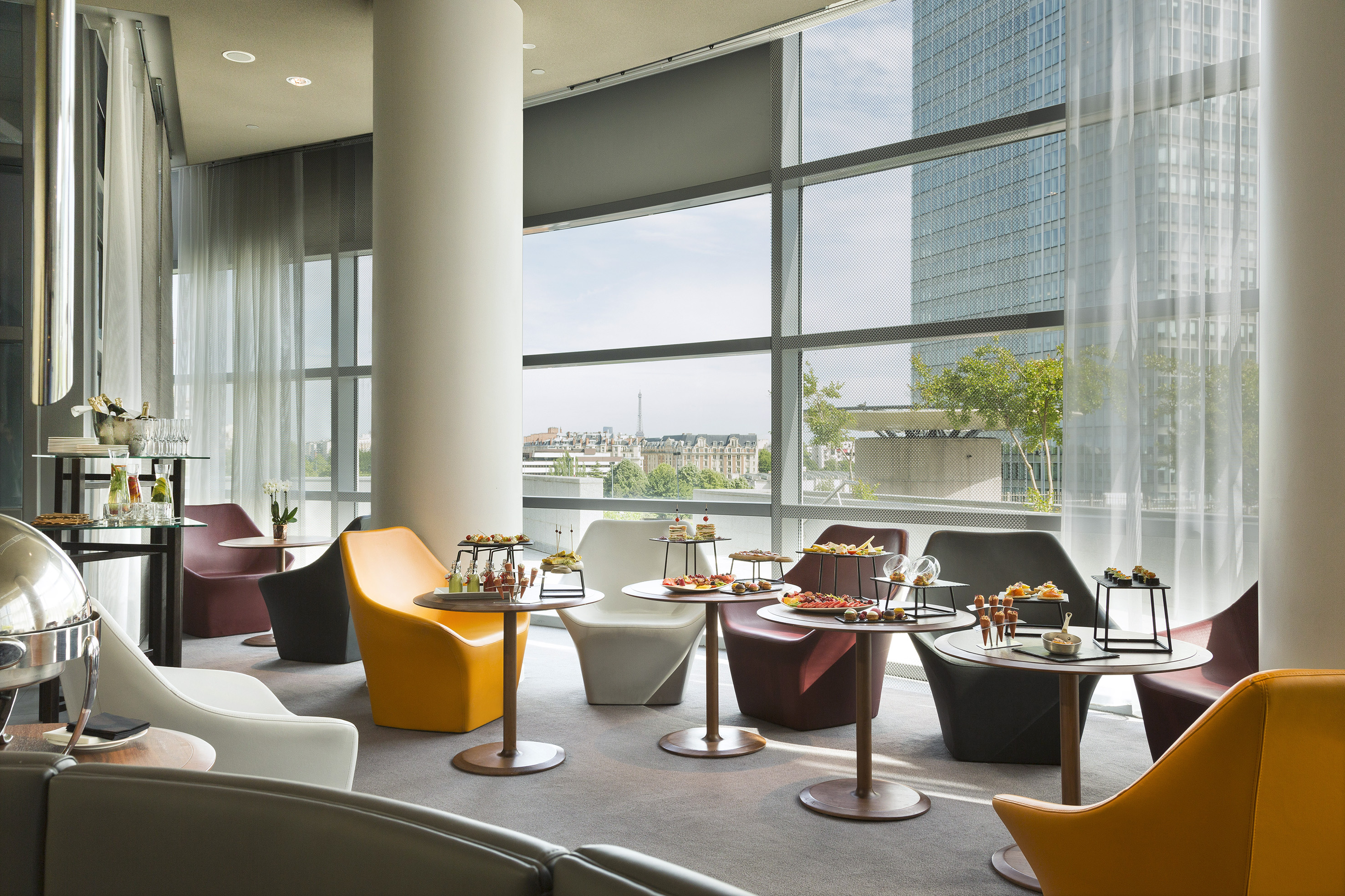 Modern event lounge with Paris city view, colorful chairs, and appetizer buffet.