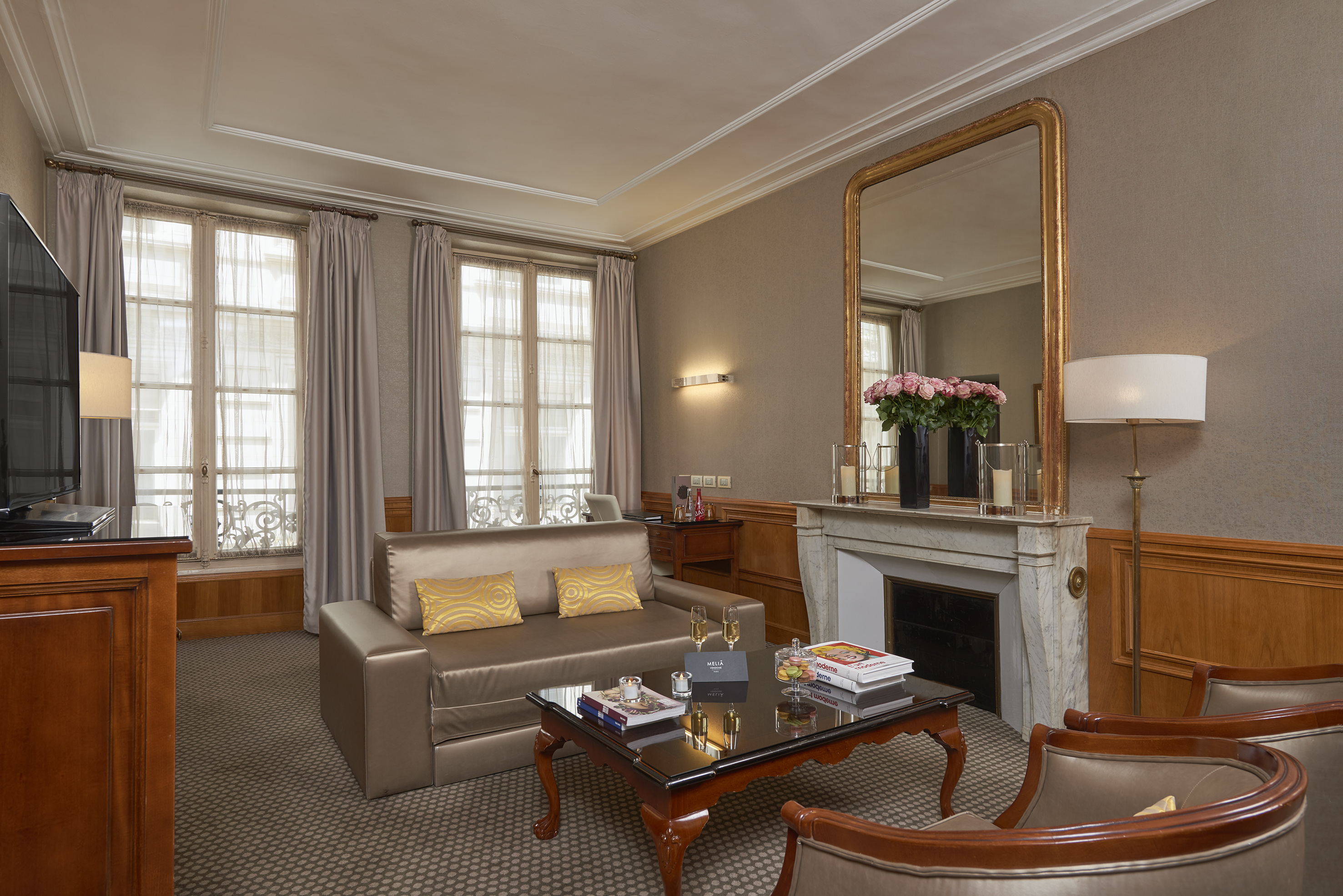 Elegant hotel suite living room with sofa, coffee table, fireplace, and gilded mirror.
