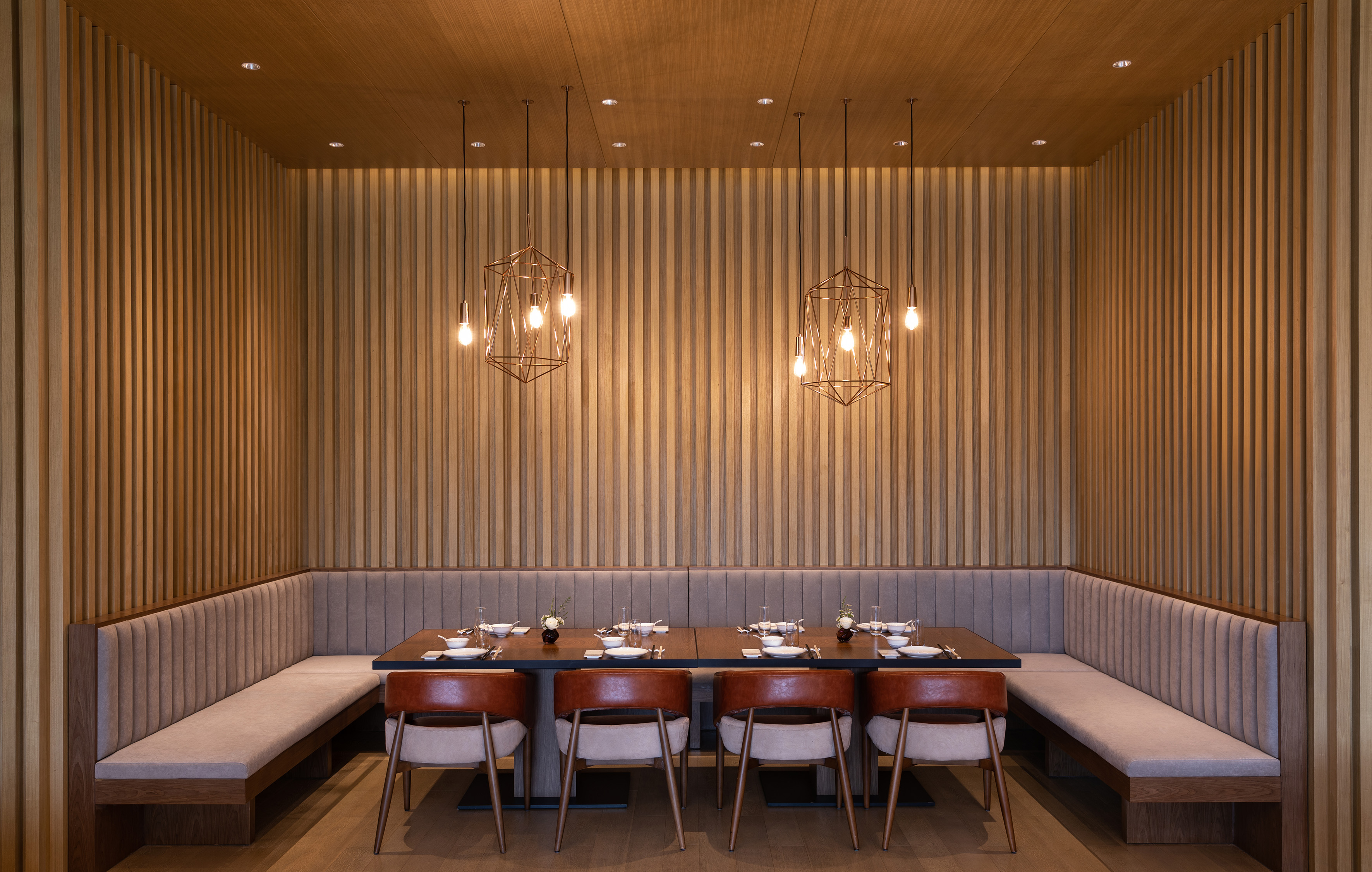 Wood-paneled restaurant dining with modern booth seating, table, and pendant lights.