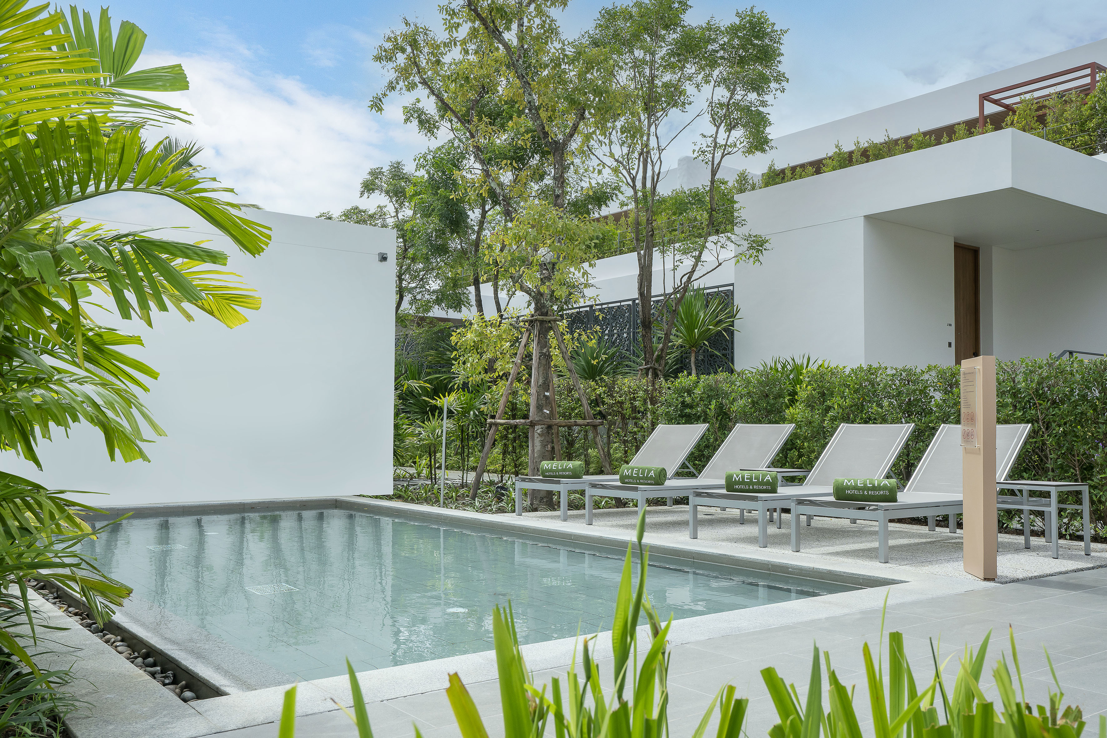 Modern resort swimming pool with lounge chairs, tropical plants, and Melia branding.