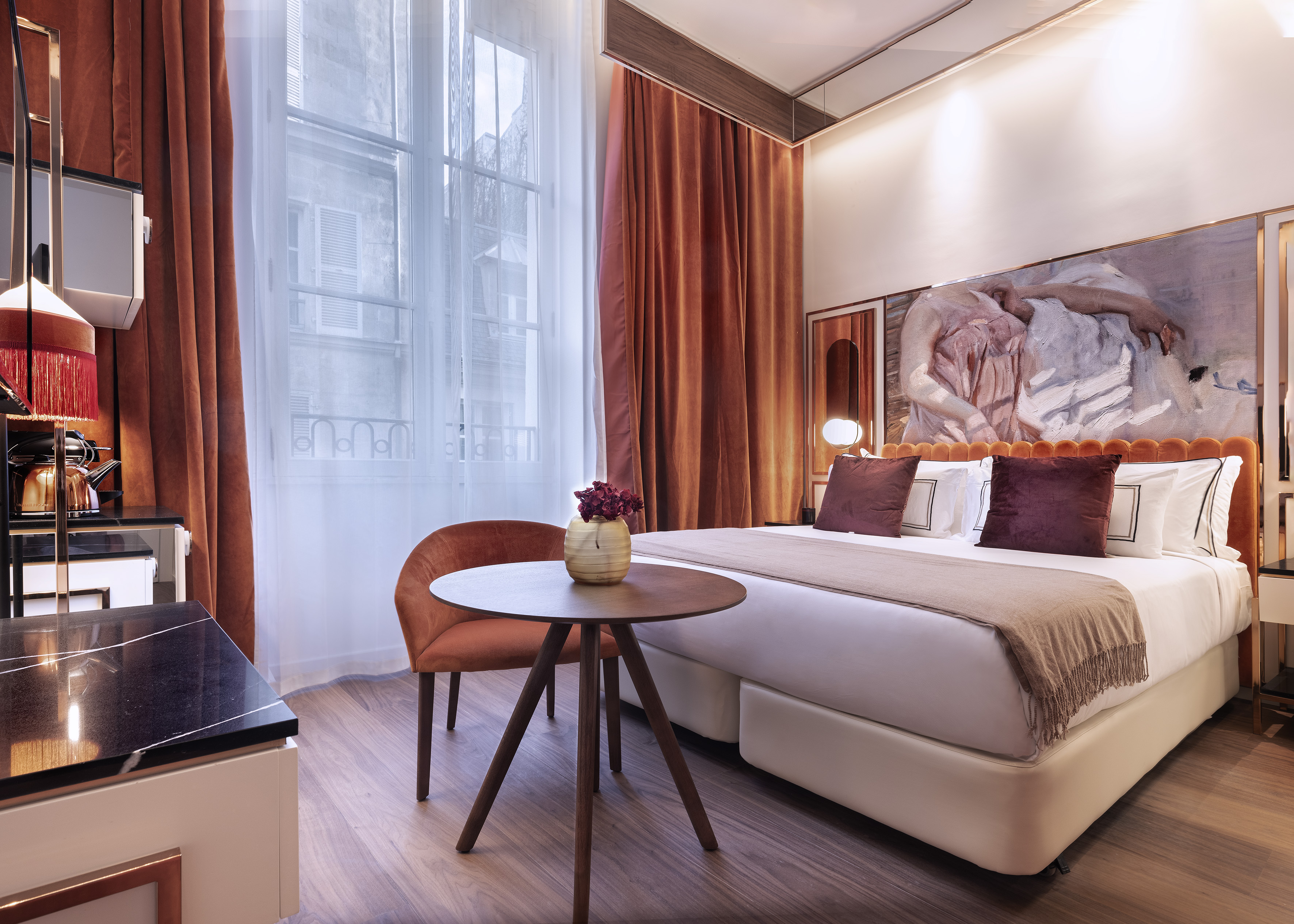 Modern luxury hotel bedroom with orange velvet, plush bed, and contemporary art.