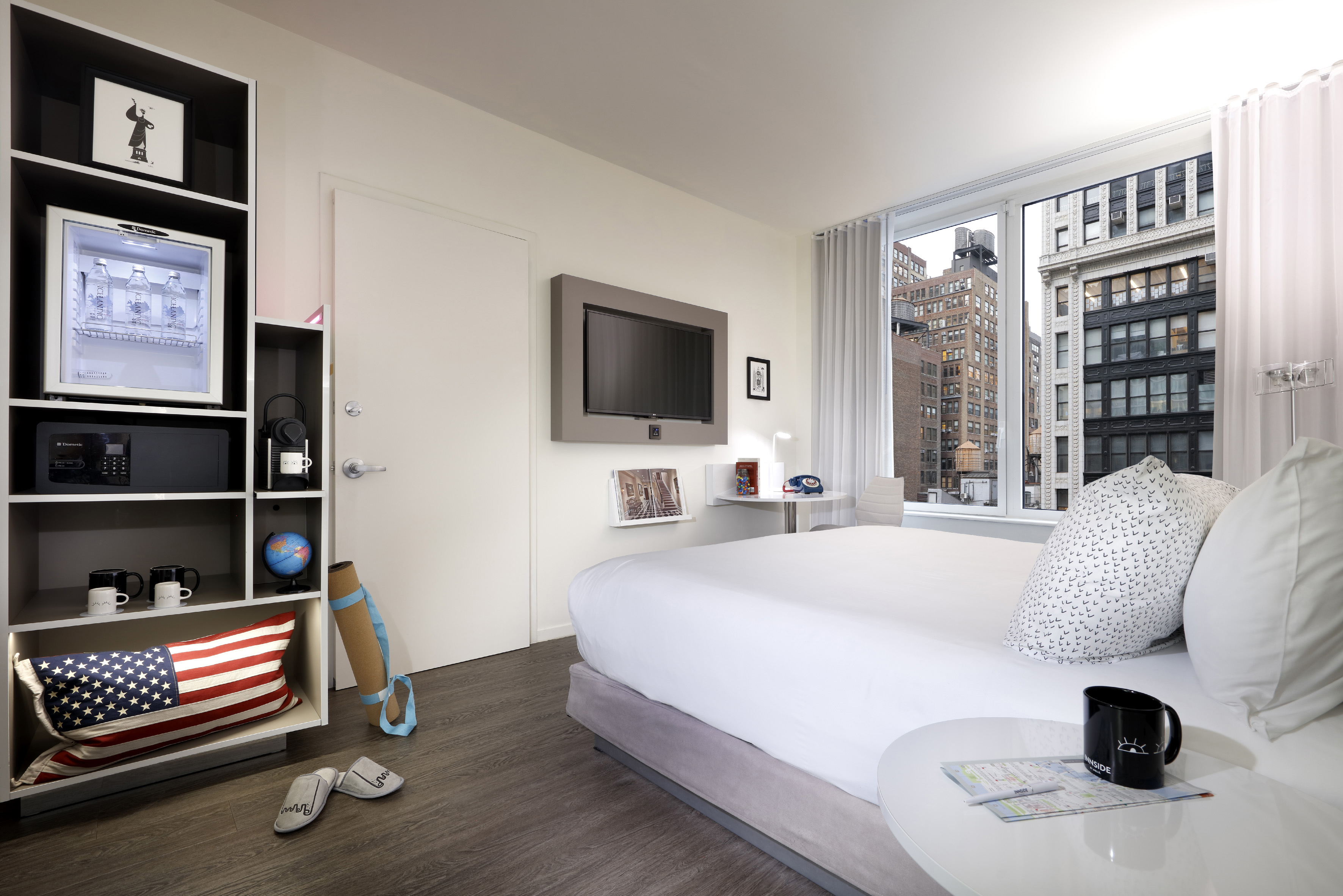 Modern hotel room with large bed, city view window, wall-mounted TV, and amenities.