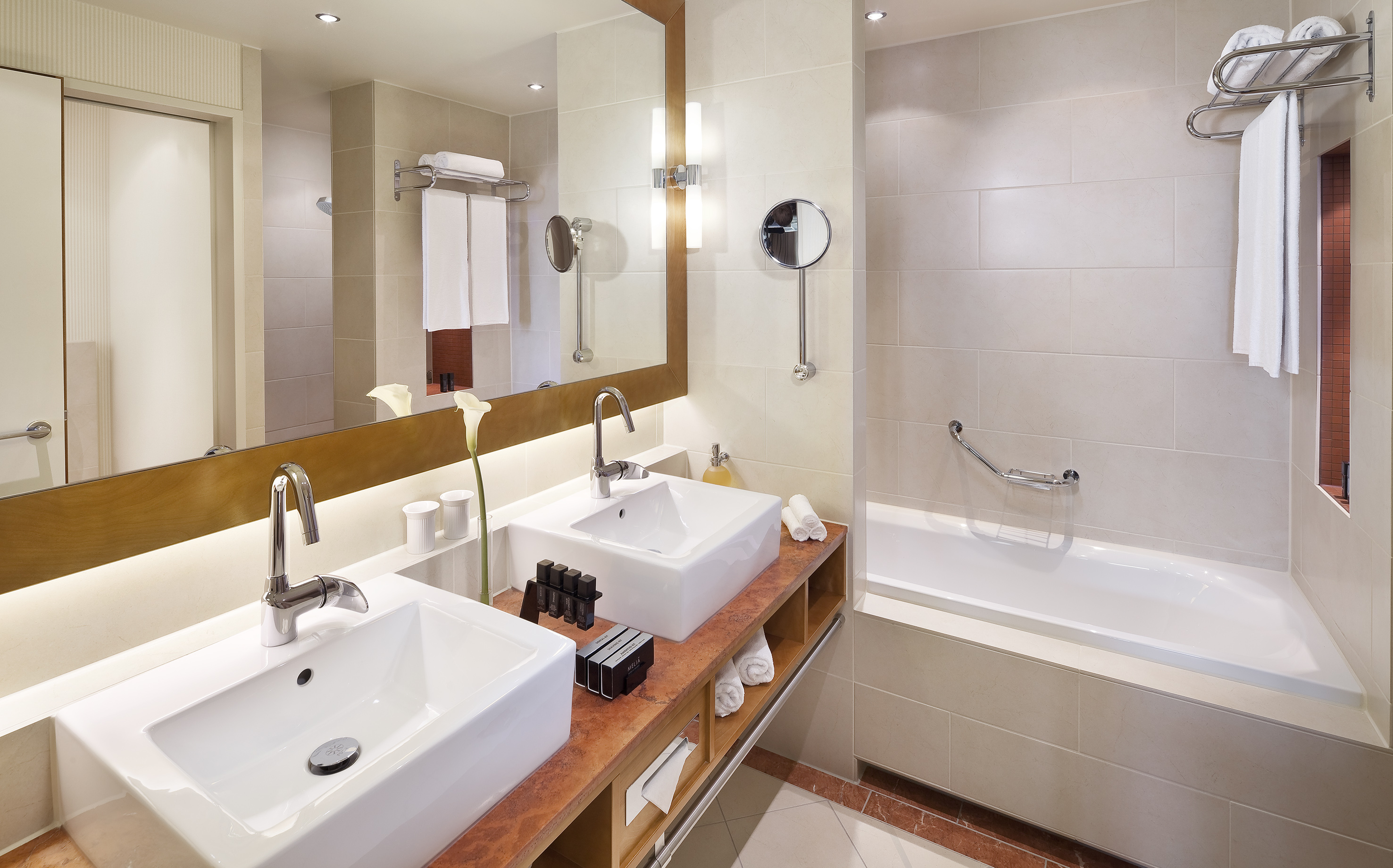 Modern hotel bathroom with double vanity, large mirror, and bathtub.