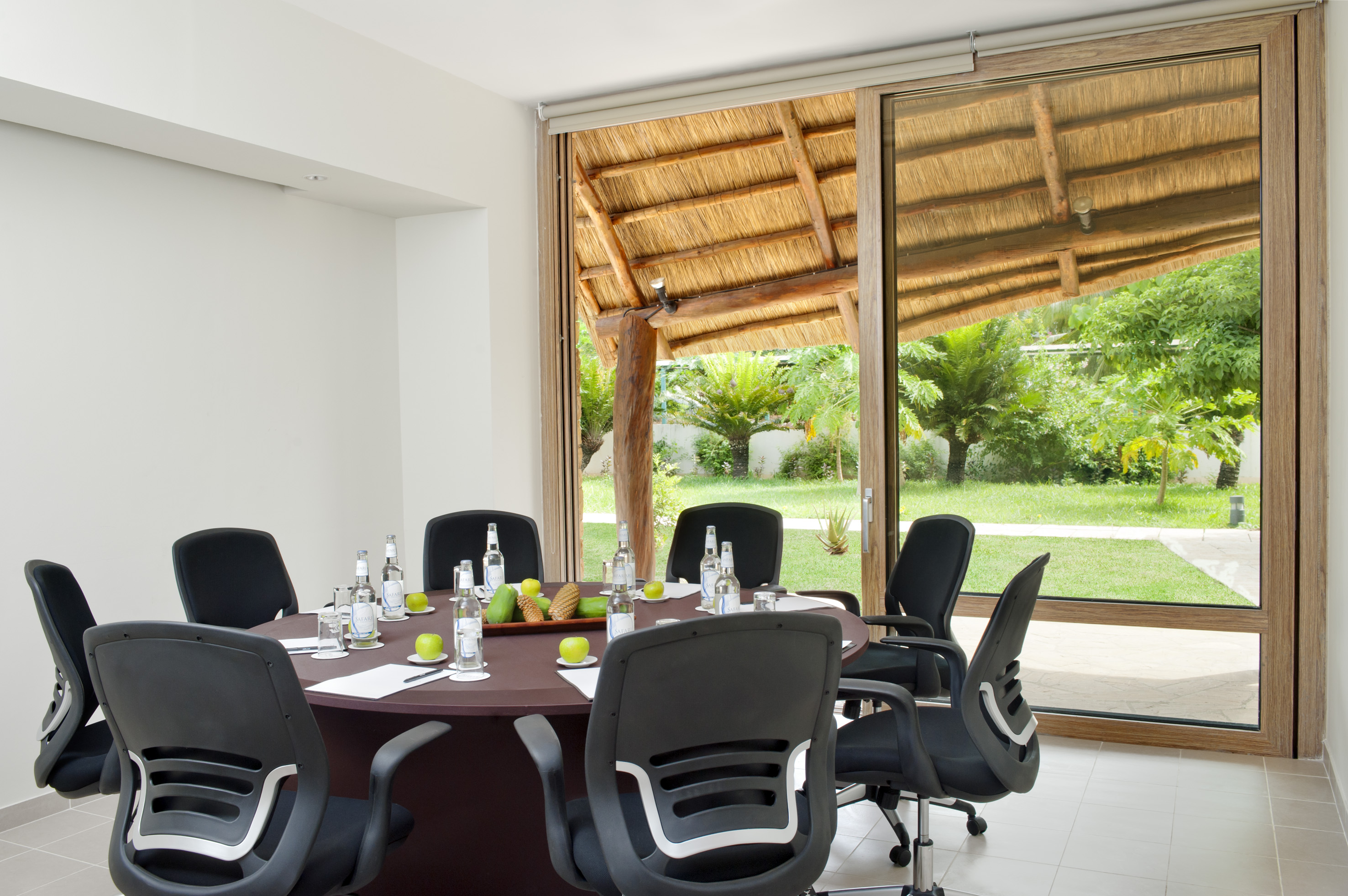 Tropical conference room with round table, chairs, and garden view.