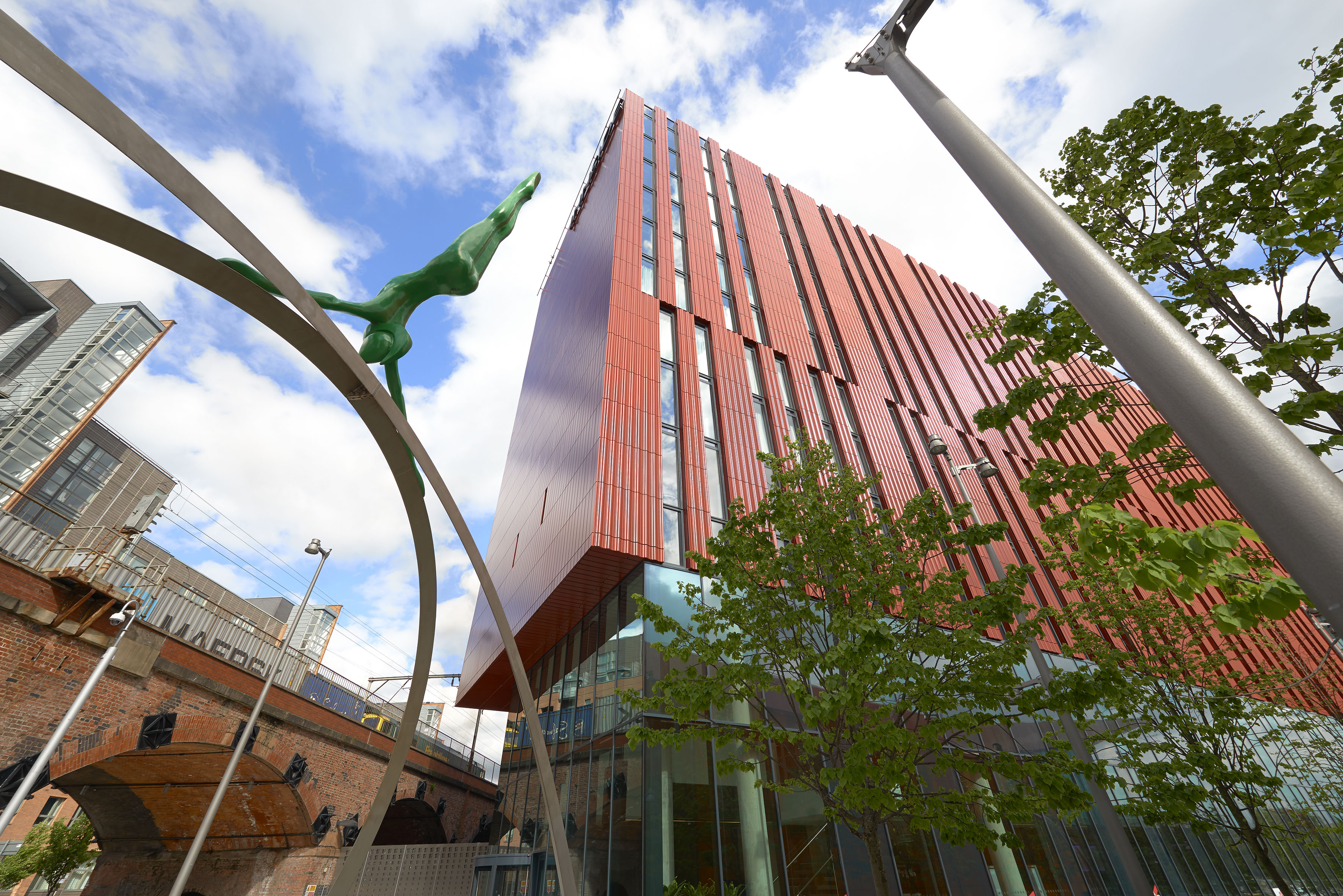 Modern red university building, green diving sculpture, brick viaduct, blue sky.