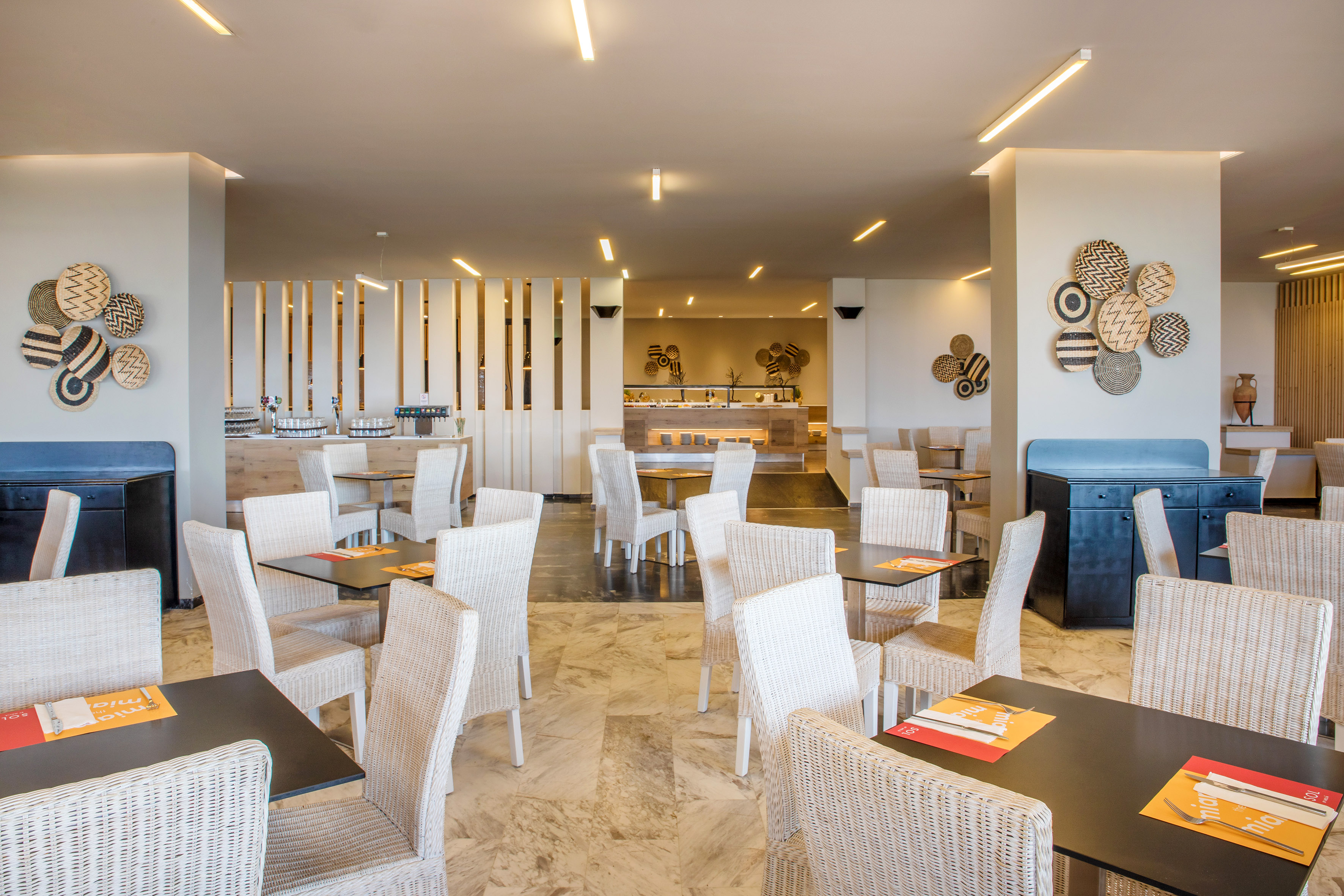 Bright modern restaurant with wicker chairs, buffet, and decorative wall art.