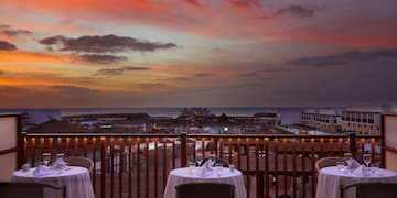 a table set up on a balcony overlooking a beach and a sunset
