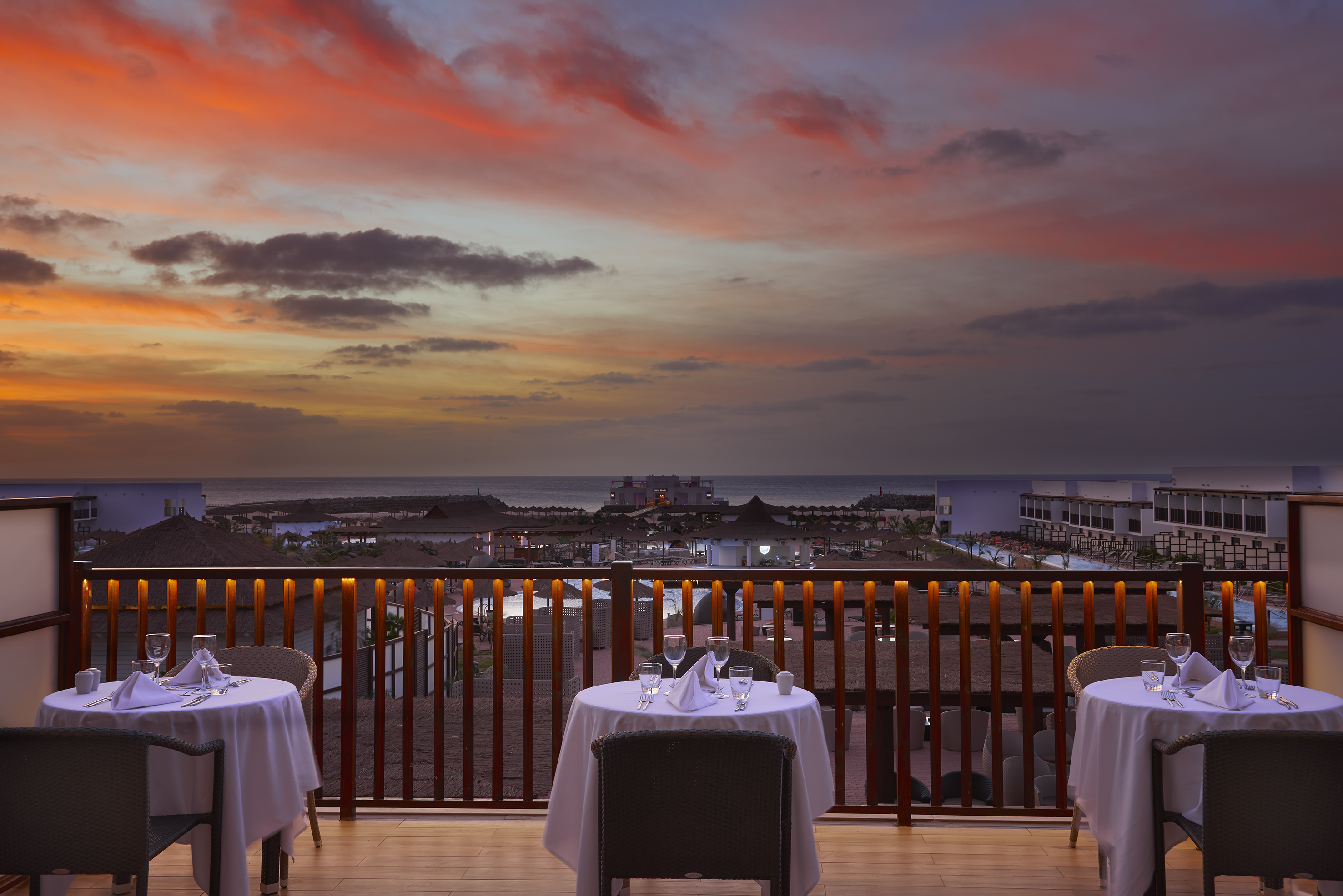 a table set up on a balcony overlooking a beach and a sunset