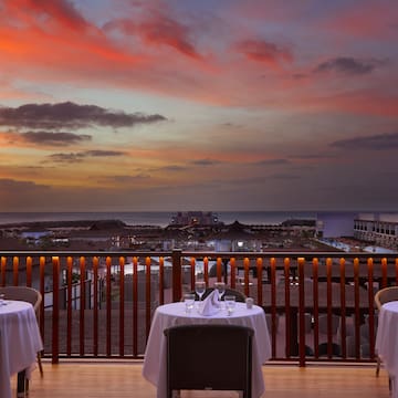 a table set up on a balcony overlooking a beach and a sunset