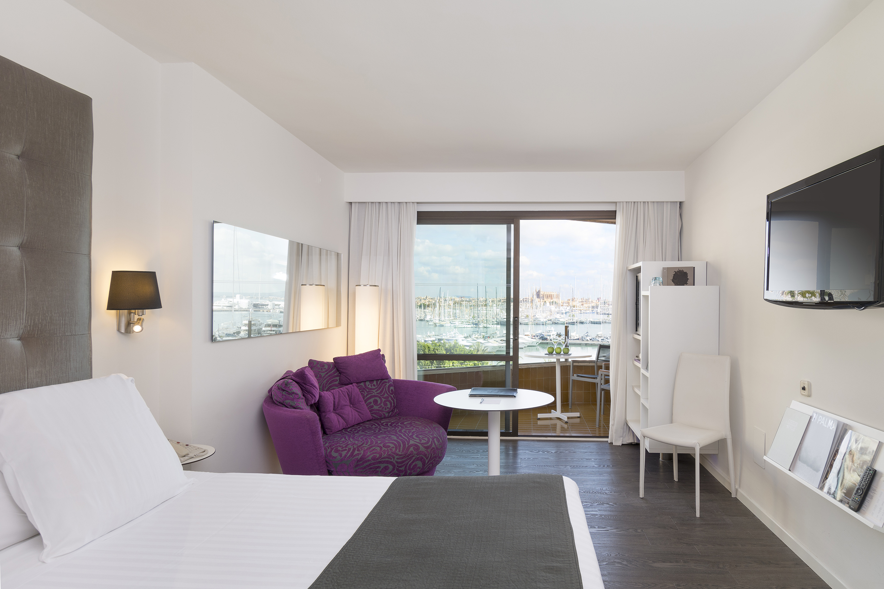 Elegant hotel room with marina view from balcony, bed, and purple armchair.