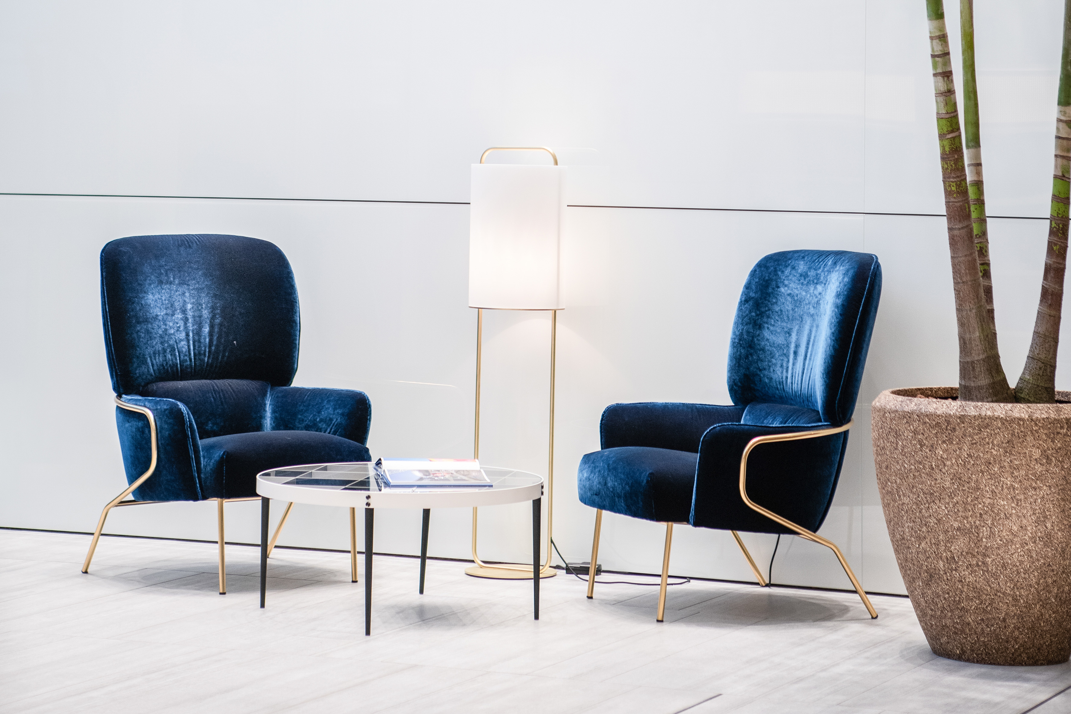 Blue velvet armchairs, coffee table, and floor lamp in a modern lounge.
