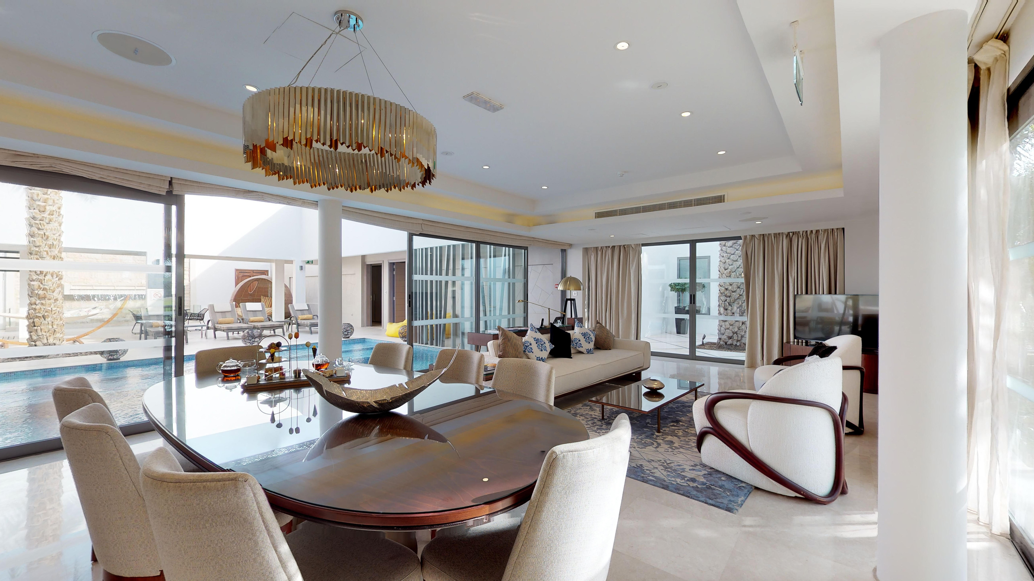 Modern luxury living/dining room, elegant chandelier, glass doors to private pool.