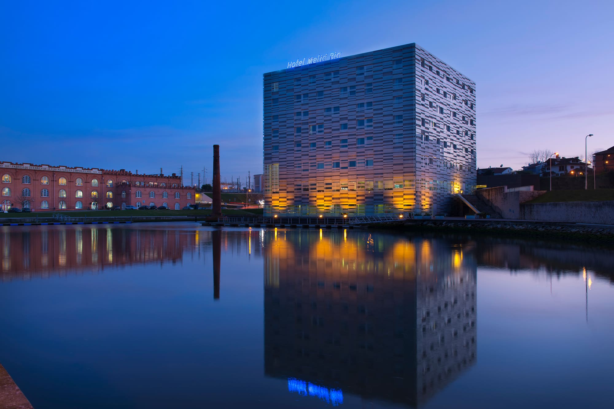 Meliá Ria Hotel and old factory reflected in water at blue hour.