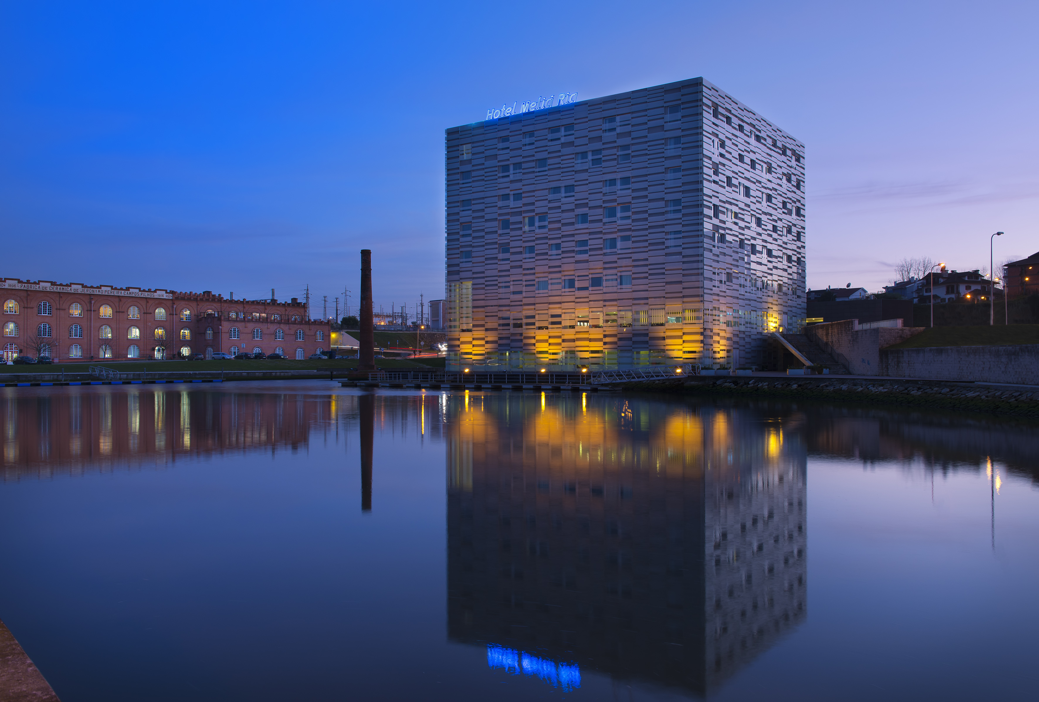 Meliá Ria Hotel and old factory reflected in water at blue hour.