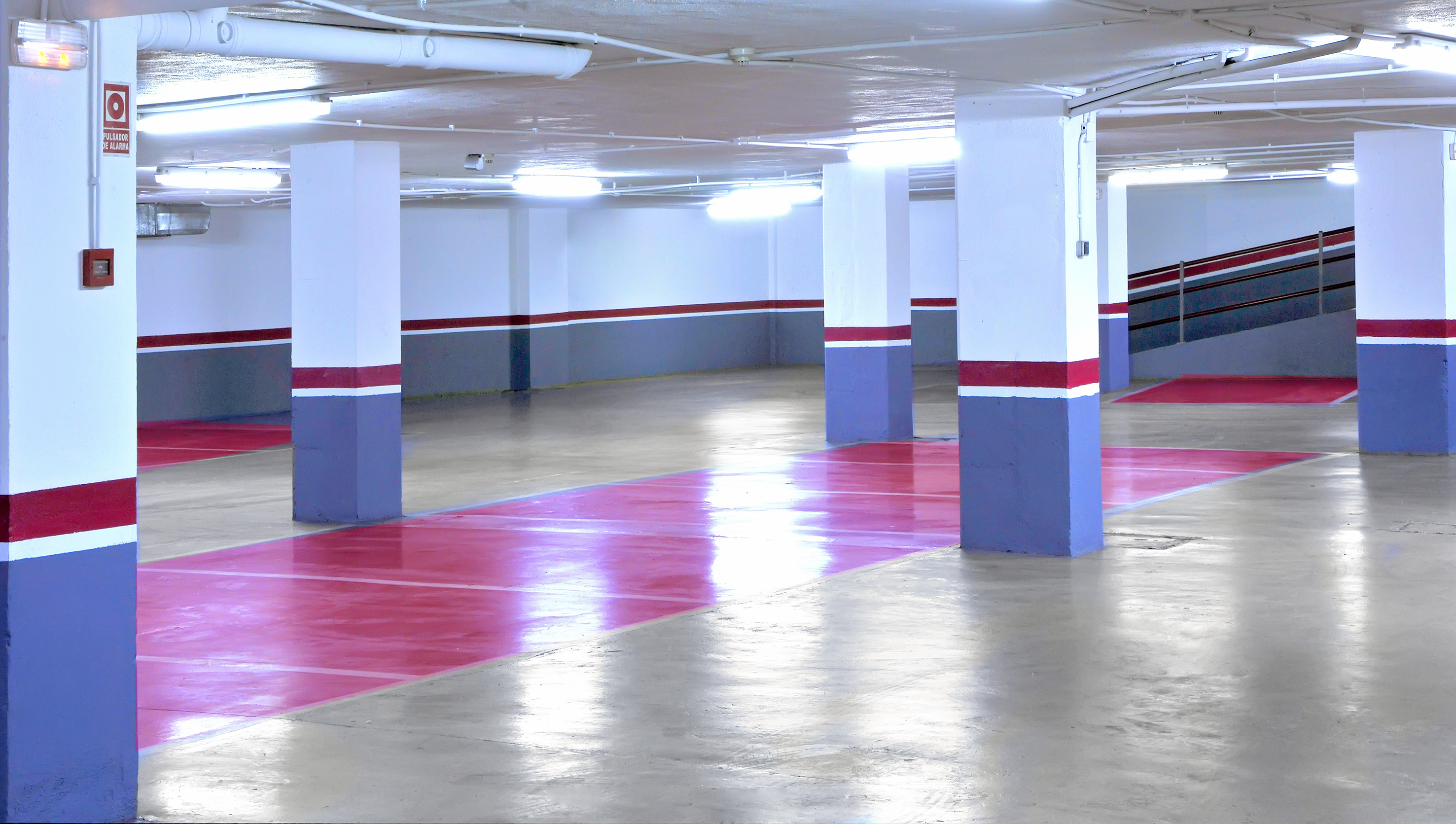 Empty underground parking garage with red parking spaces and striped columns.