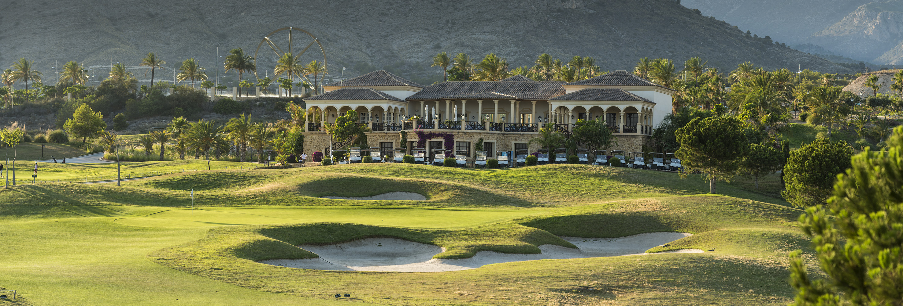 Elegant golf resort clubhouse with parked golf carts and green course bunkers.