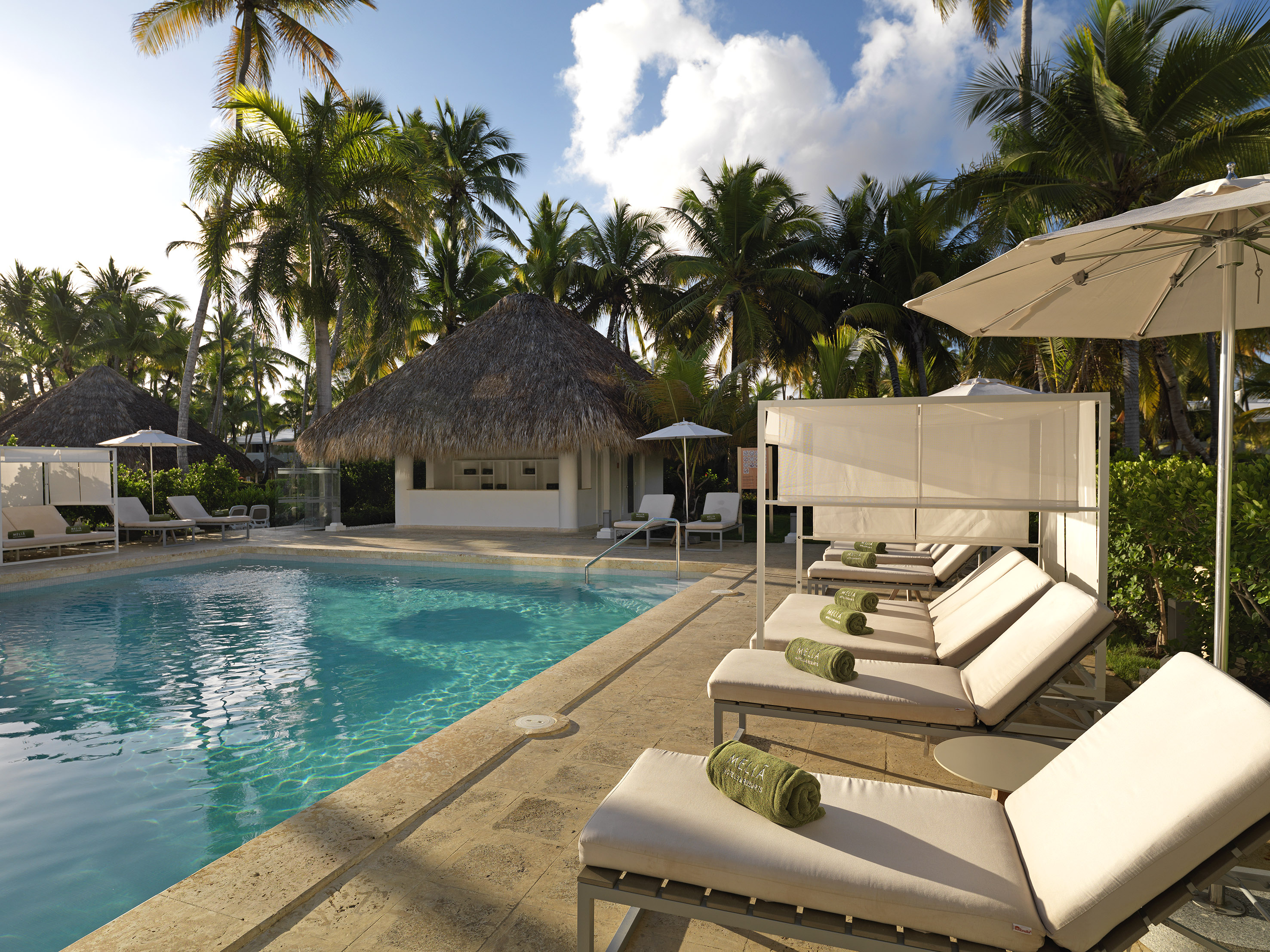 Luxury hotel pool area with sun loungers, umbrellas, and lush palm trees.