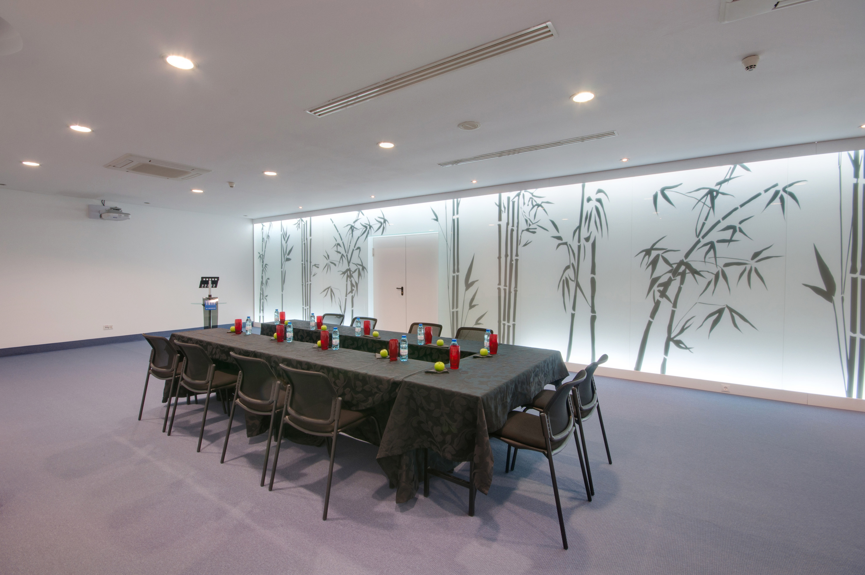 Conference room with long table, chairs, projector, and bamboo accent wall.