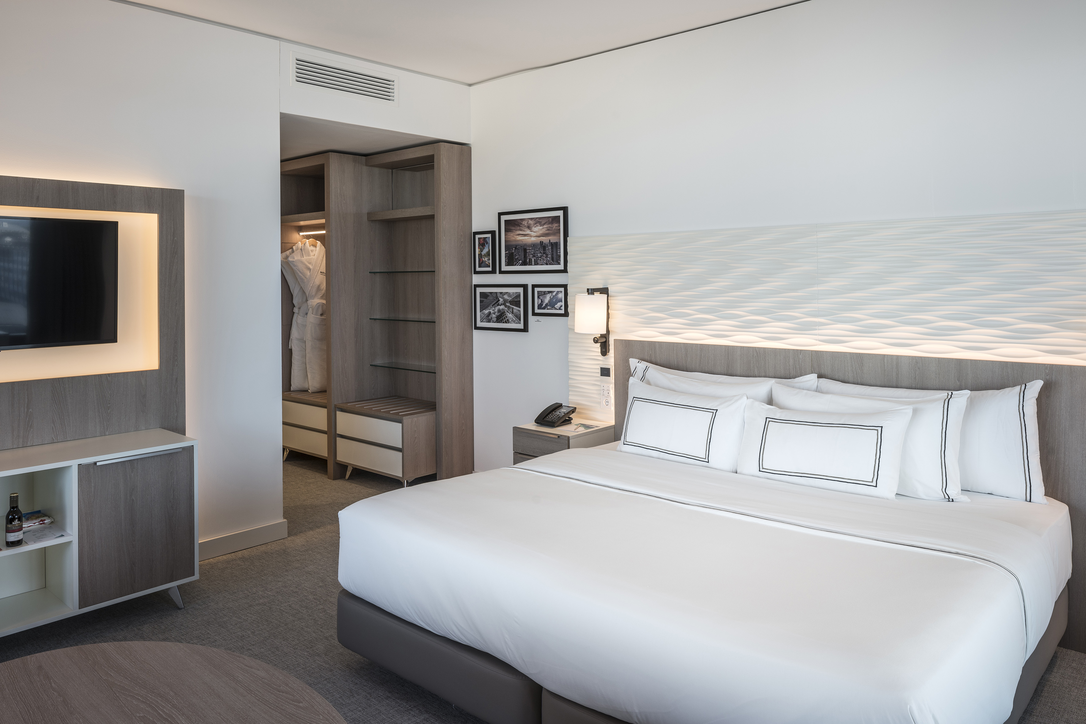 Modern hotel bedroom with large bed, wall TV, and integrated wardrobe.