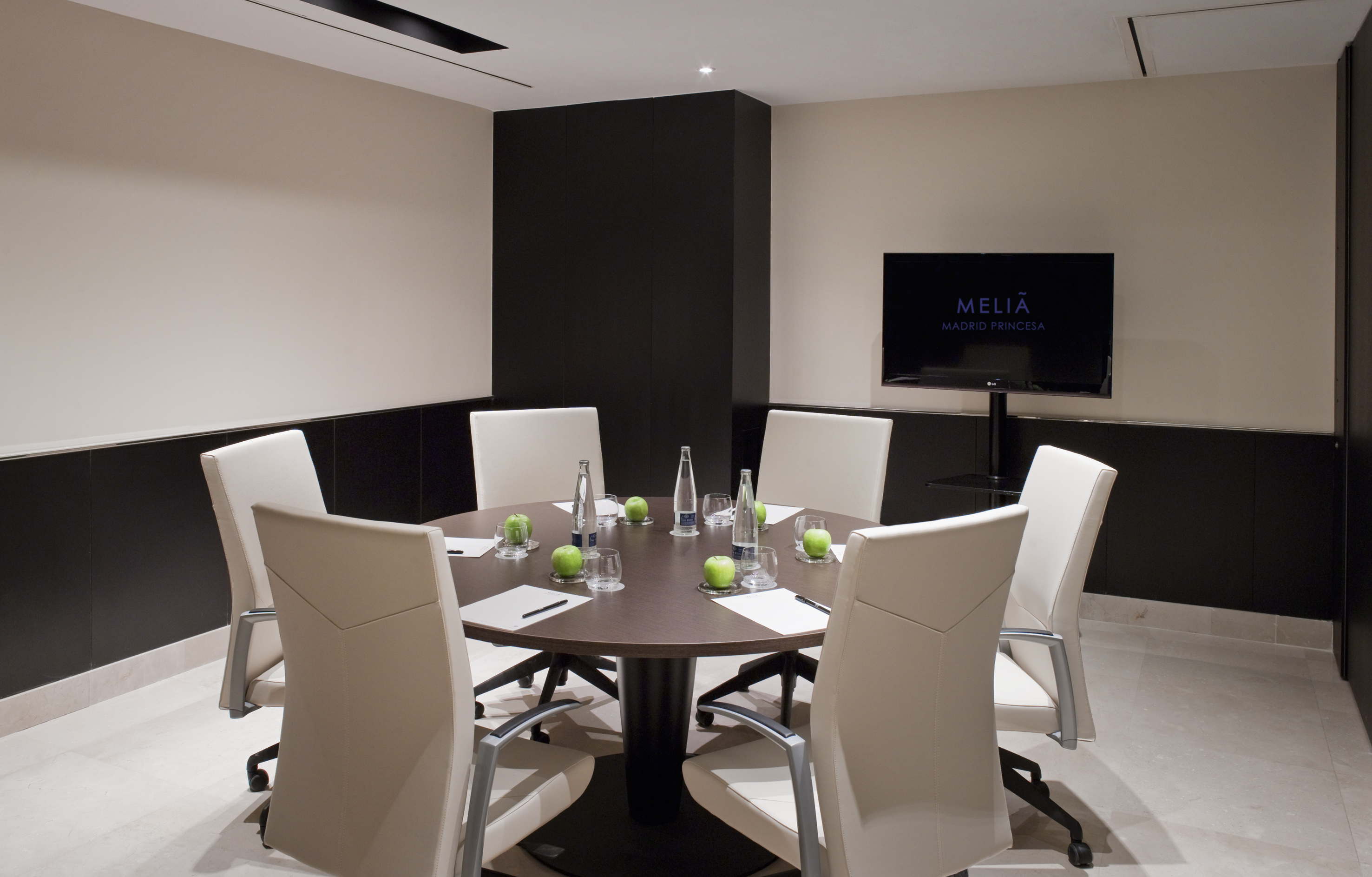 Meliá Madrid Princesa hotel meeting room, round table, cream chairs, TV display.