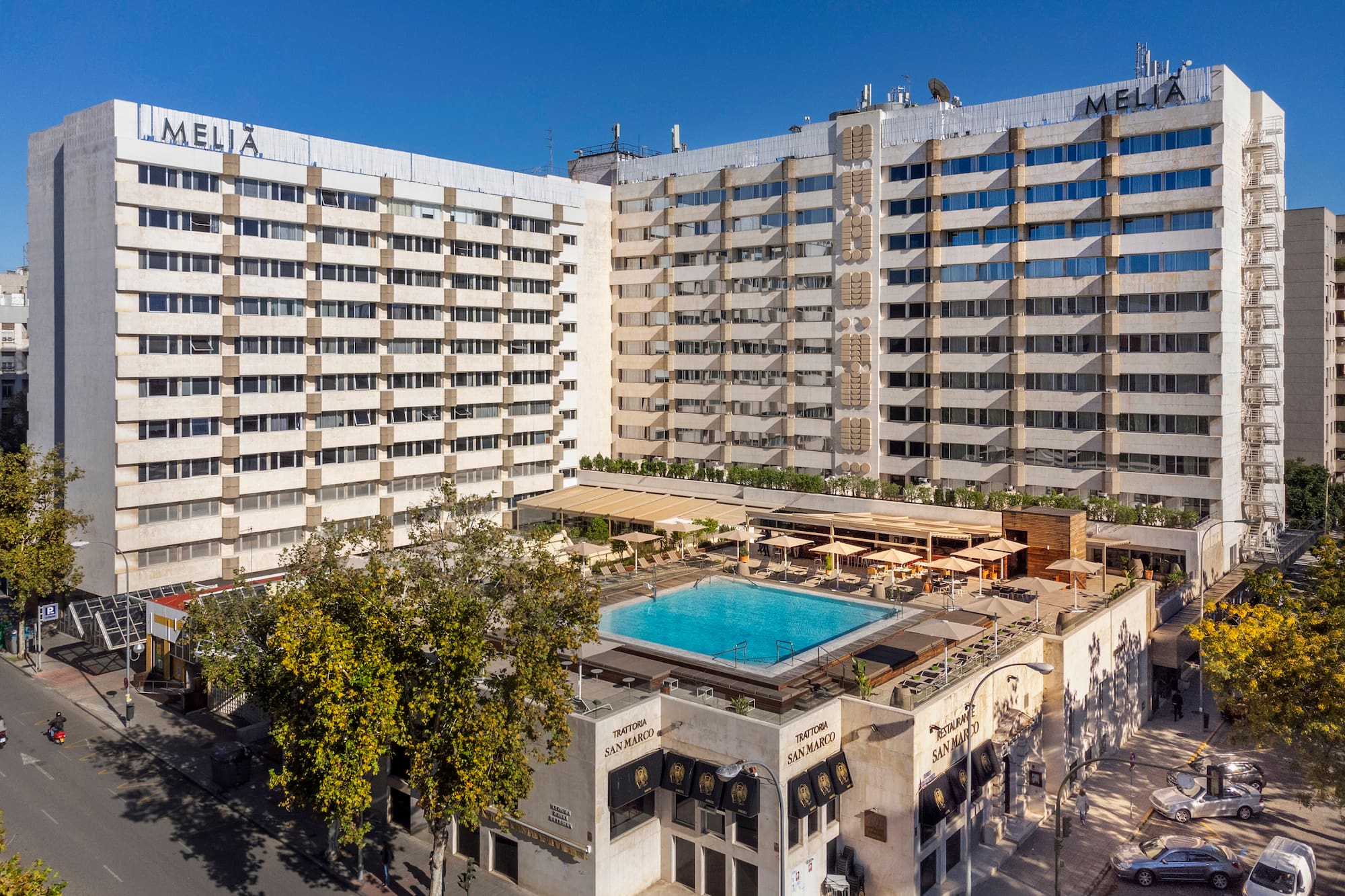Melia hotel building with rooftop pool, sunny terrace, and street scene.