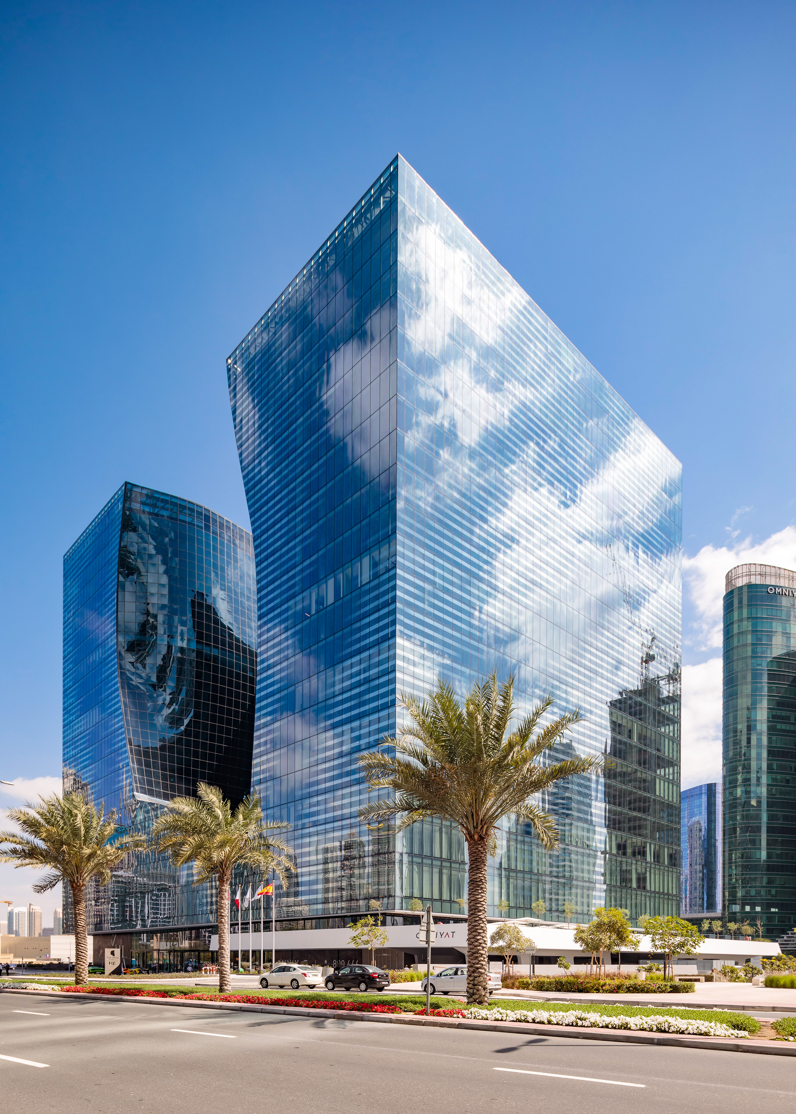 Modern glass skyscrapers reflecting blue sky and clouds with palm trees.