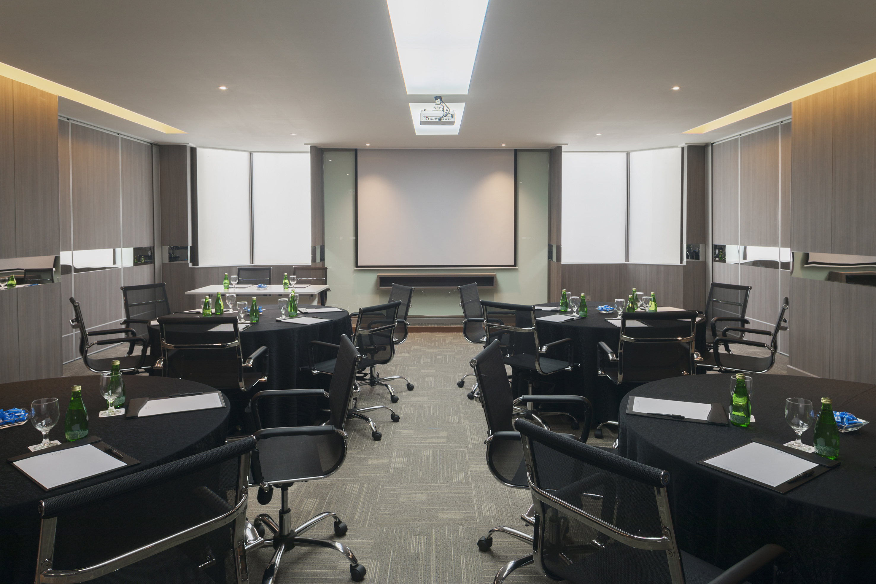Conference room with round tables, chairs, projector screen, ready for business meetings.