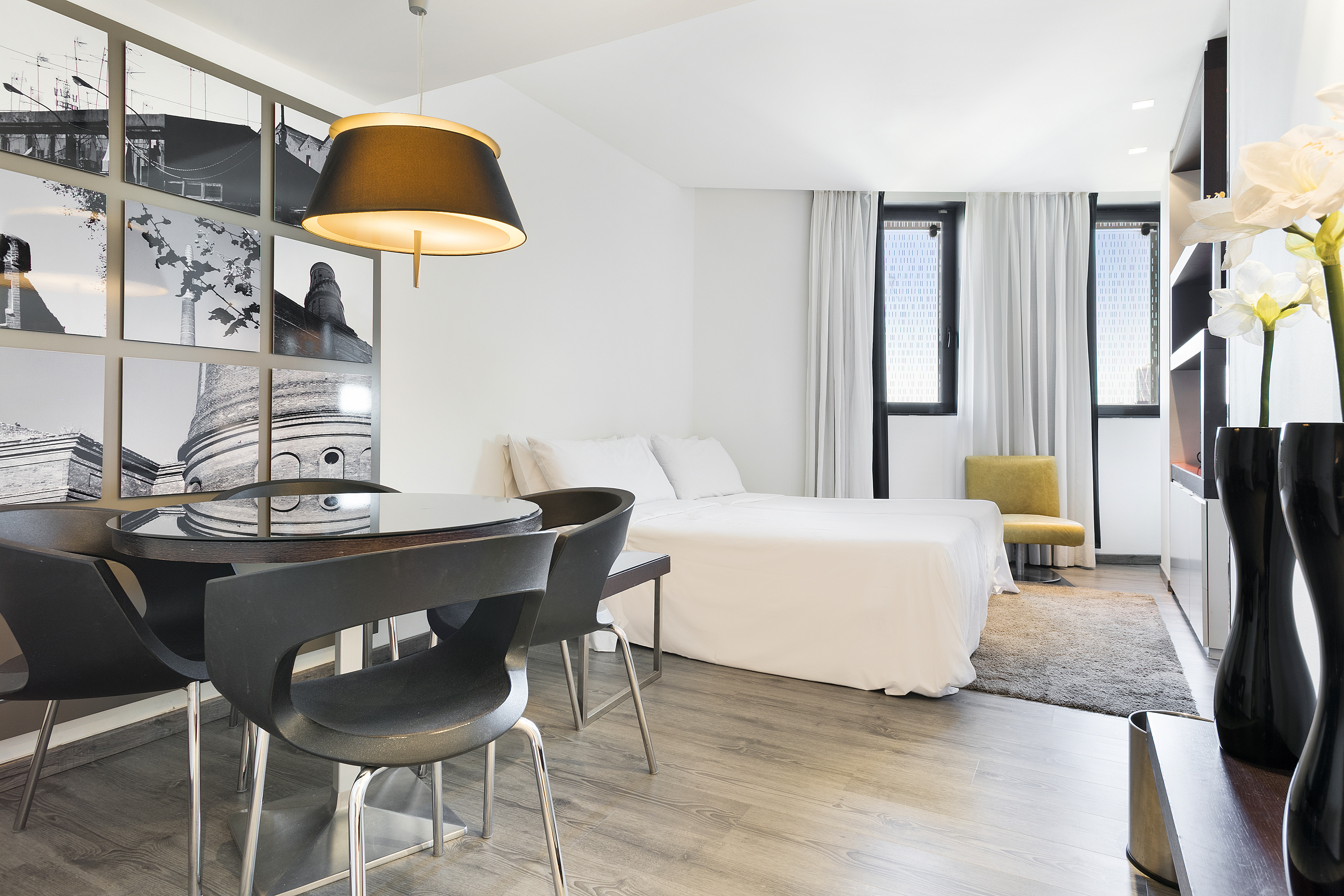 Modern studio apartment with dining area, white bed, and black & white wall art.