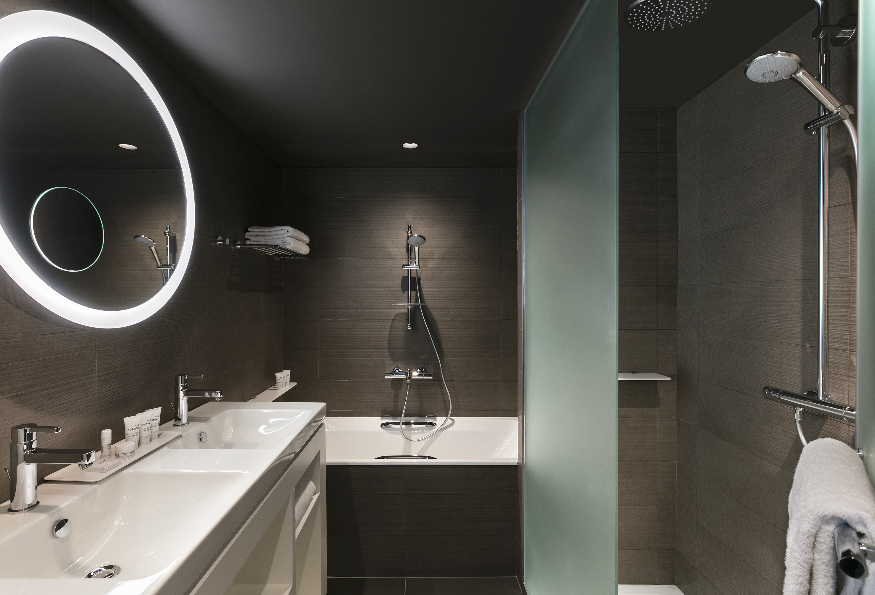 Modern bathroom with double vanity, round LED mirror, and combined bath & shower.
