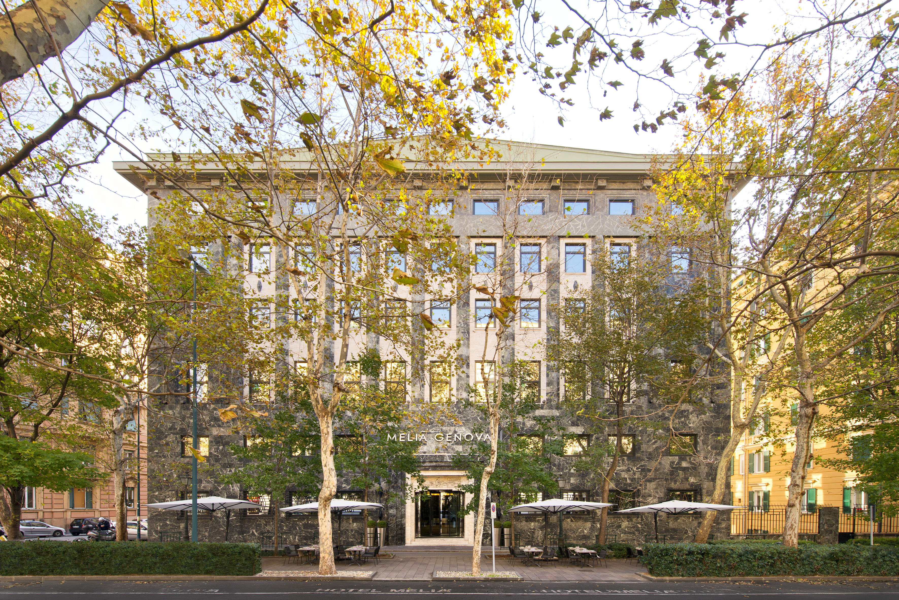 Melia Genova hotel, dark stone facade, autumn trees, outdoor cafe, Genoa.