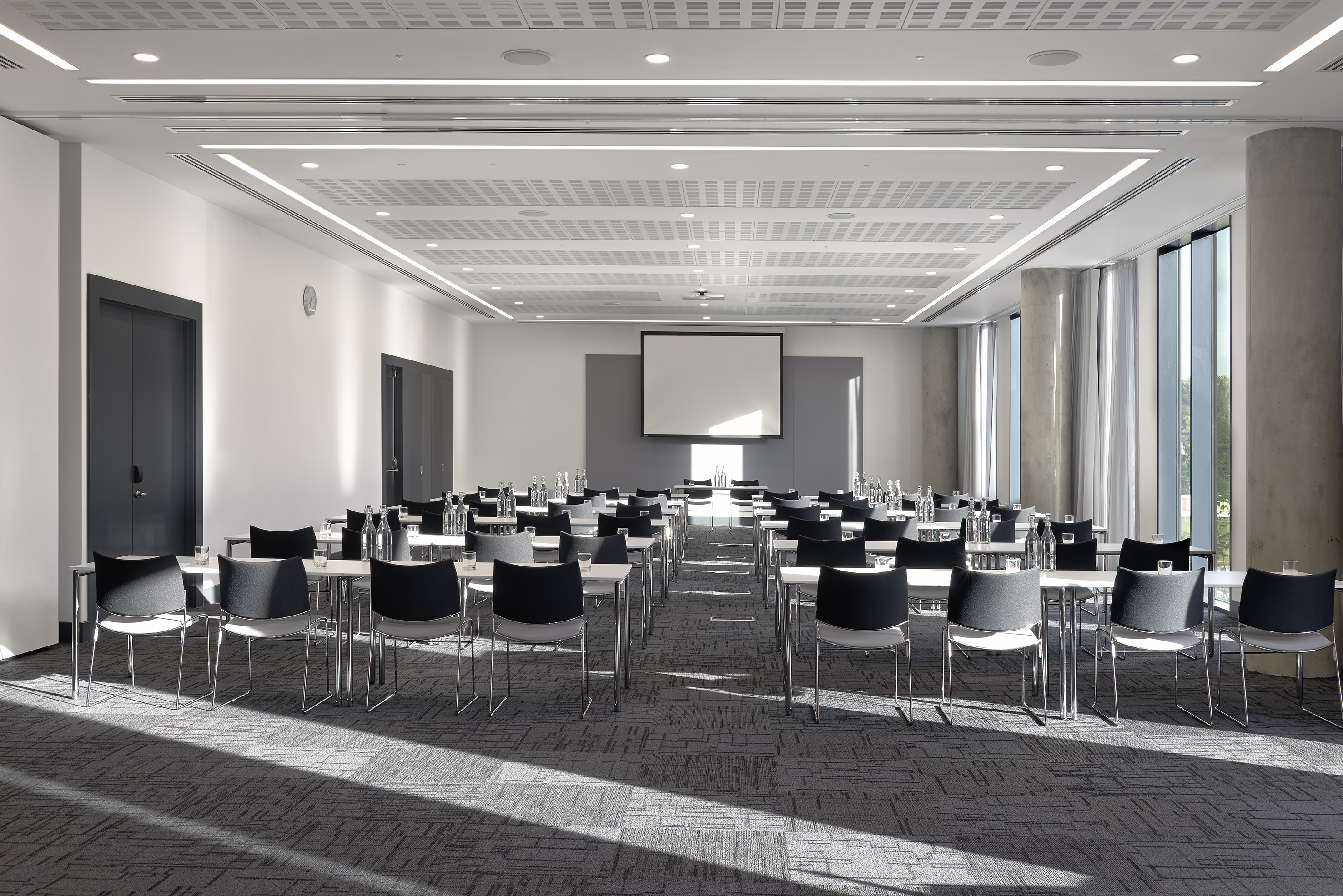 Modern conference room with tables, chairs, projector screen, and large windows.