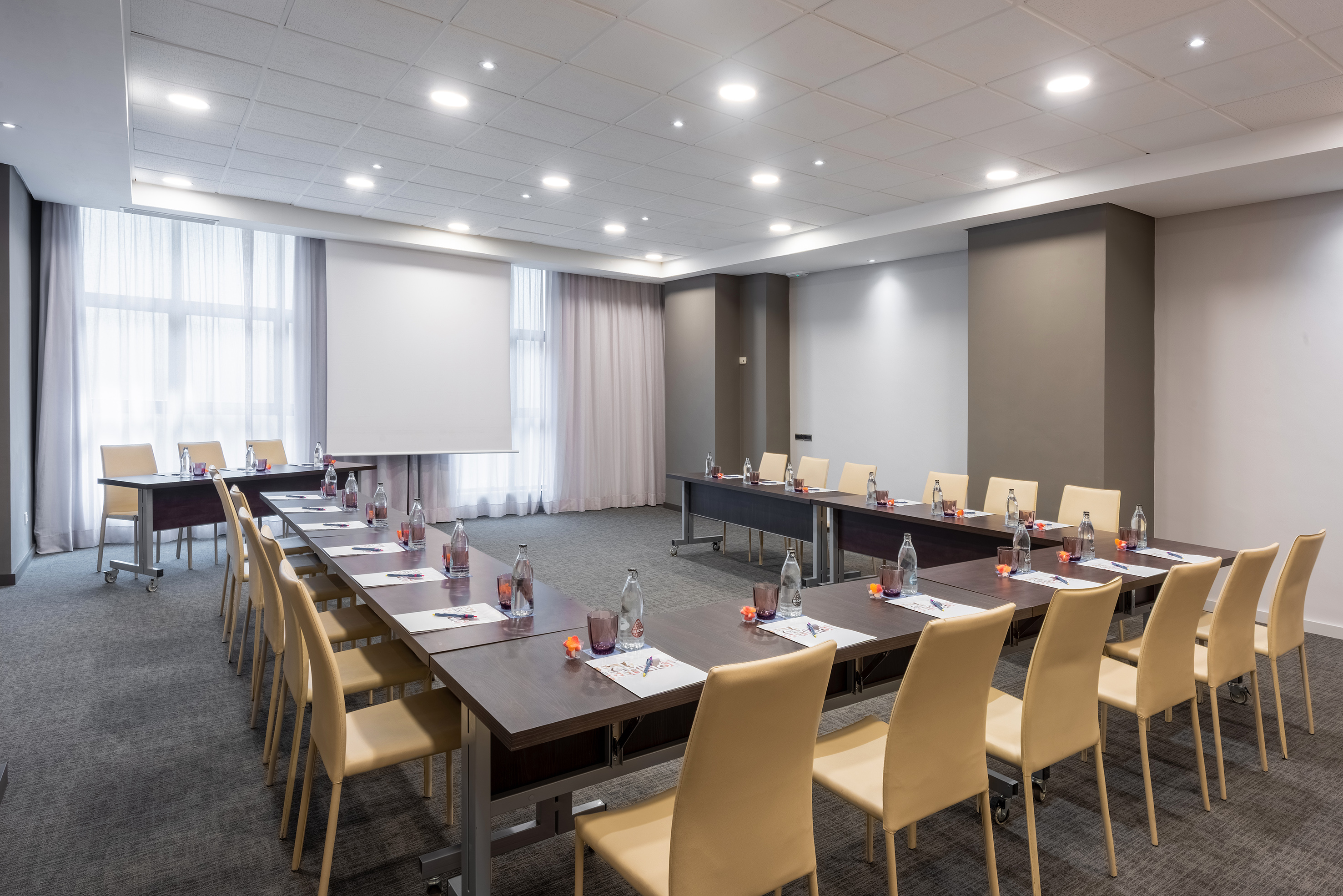 Conference room with U-shaped table setup, beige chairs, and projector.