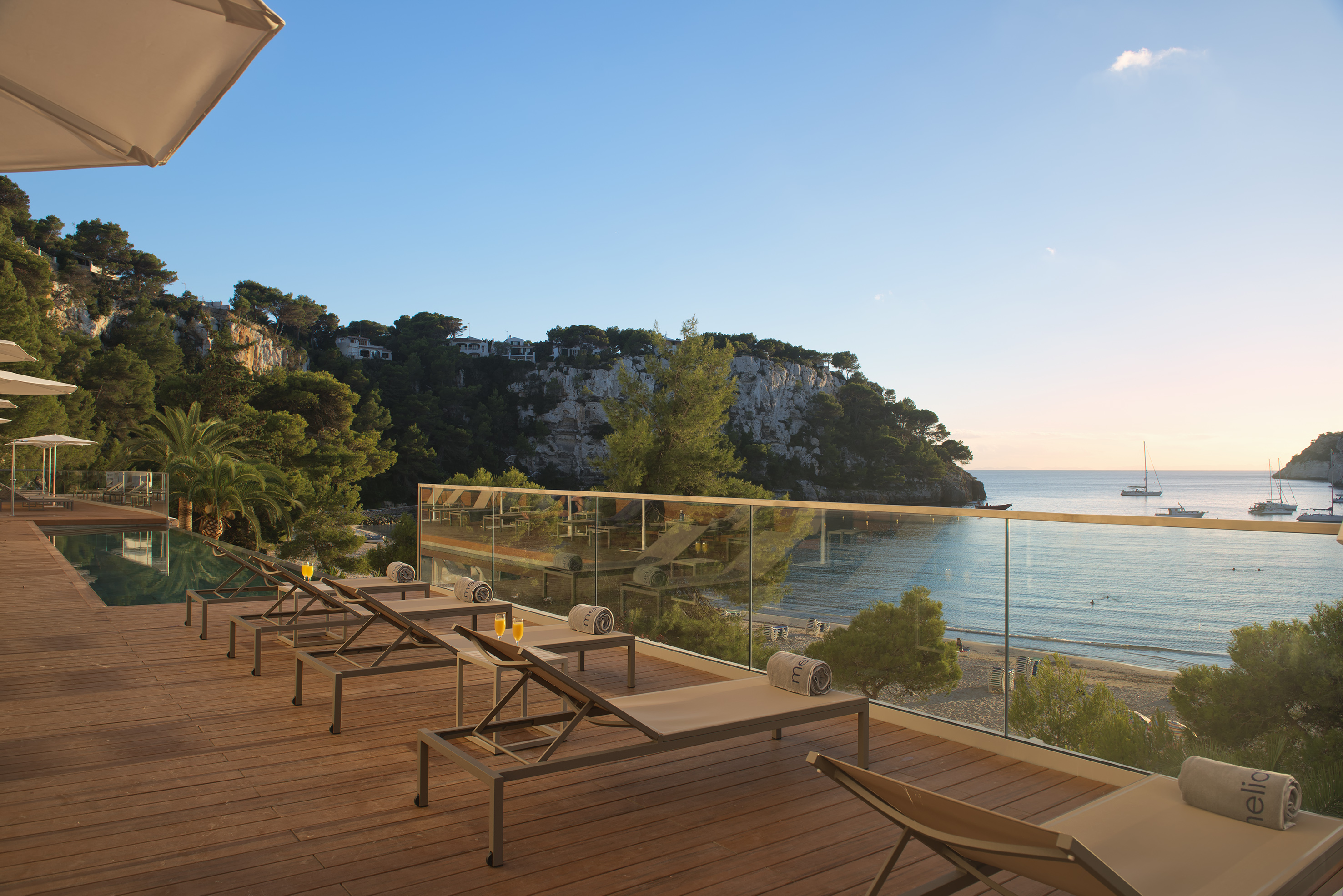 Hotel deck with sun loungers, infinity pool, overlooking beach, sea, and yachts.