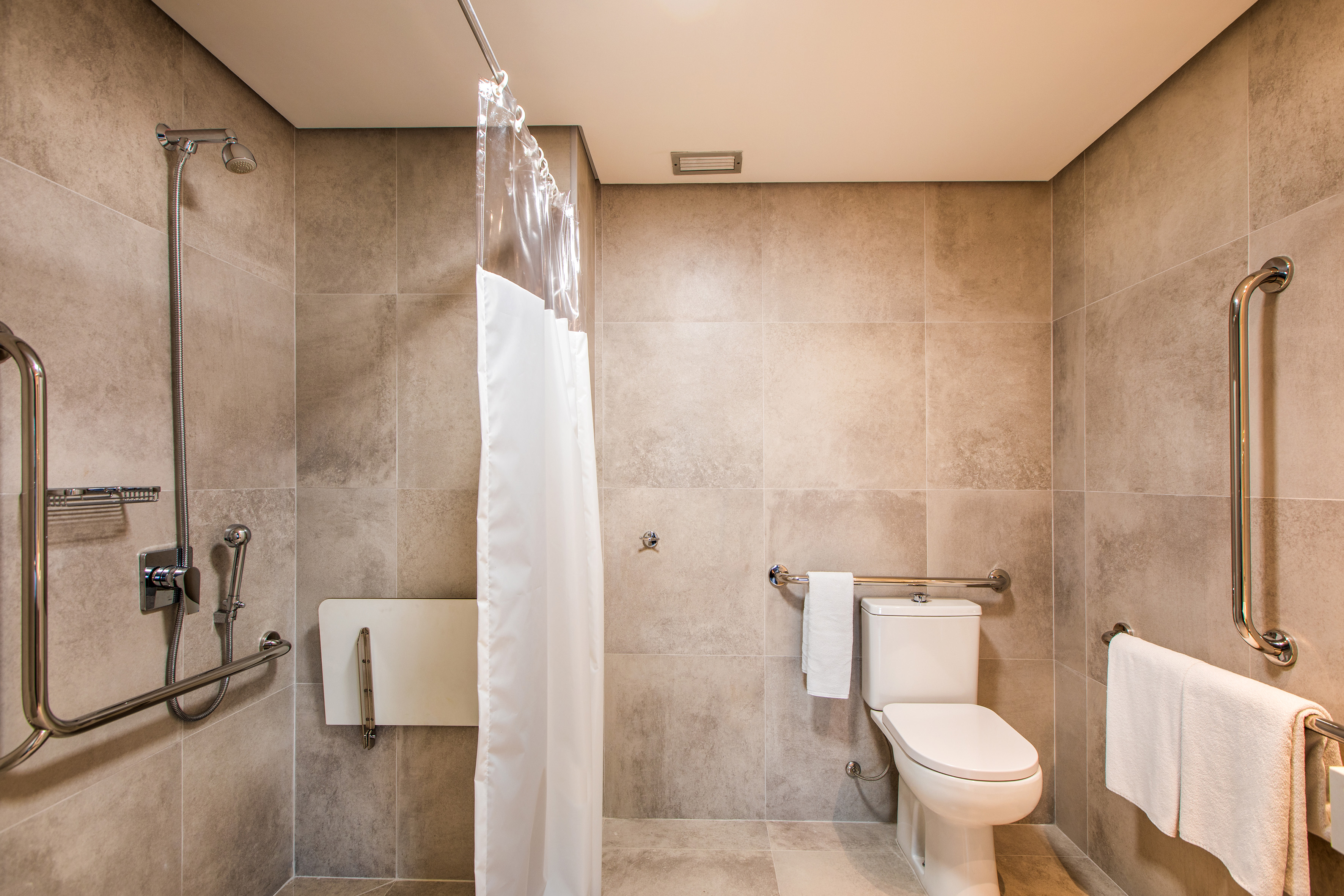 Accessible bathroom with roll-in shower, grab bars, fold-down seat, toilet.