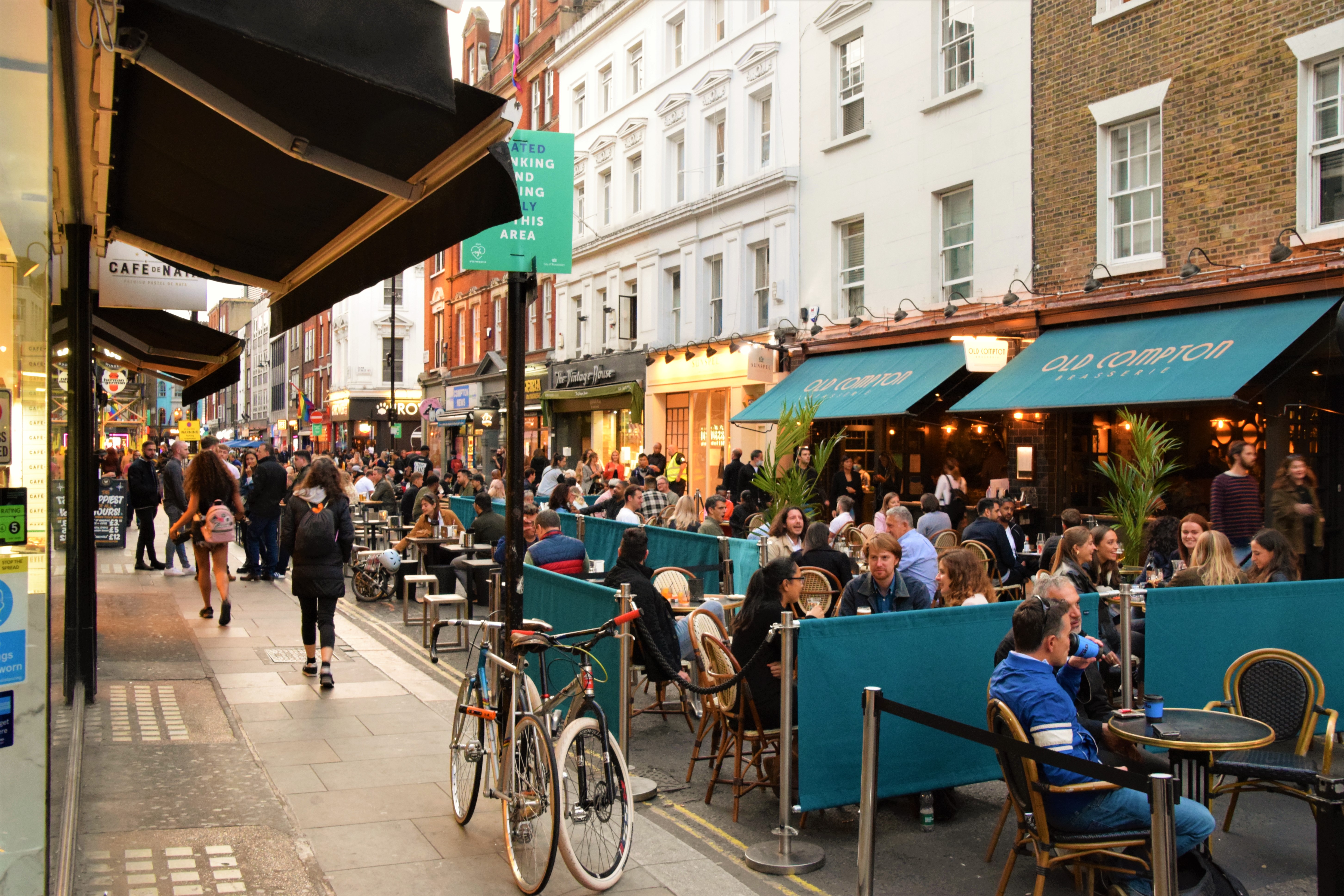 Calle concurrida Old Compton, Londres, con gente en terrazas de restaurantes.