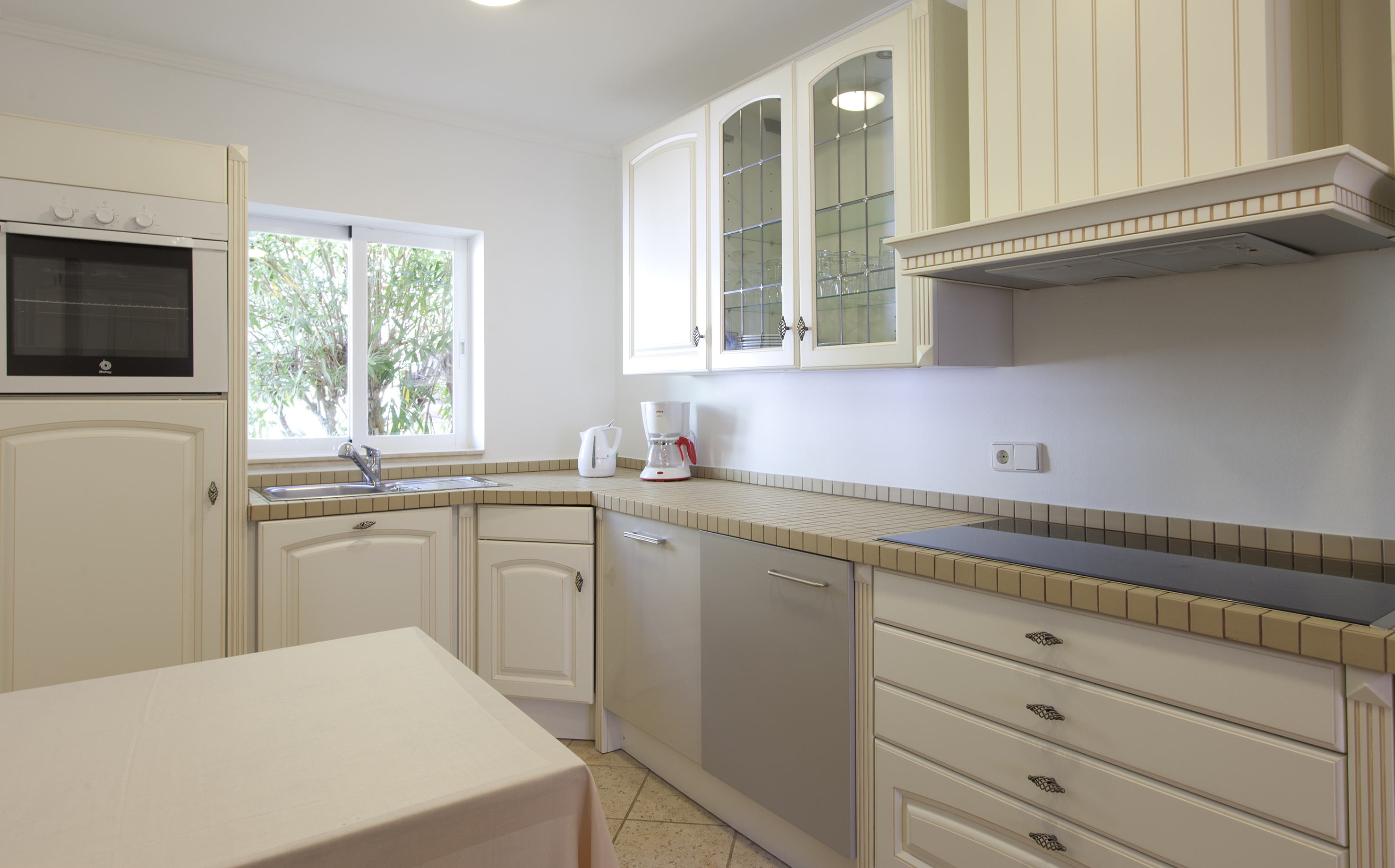 Bright modern kitchen with cream cabinets, oven, tiled counter, and window.